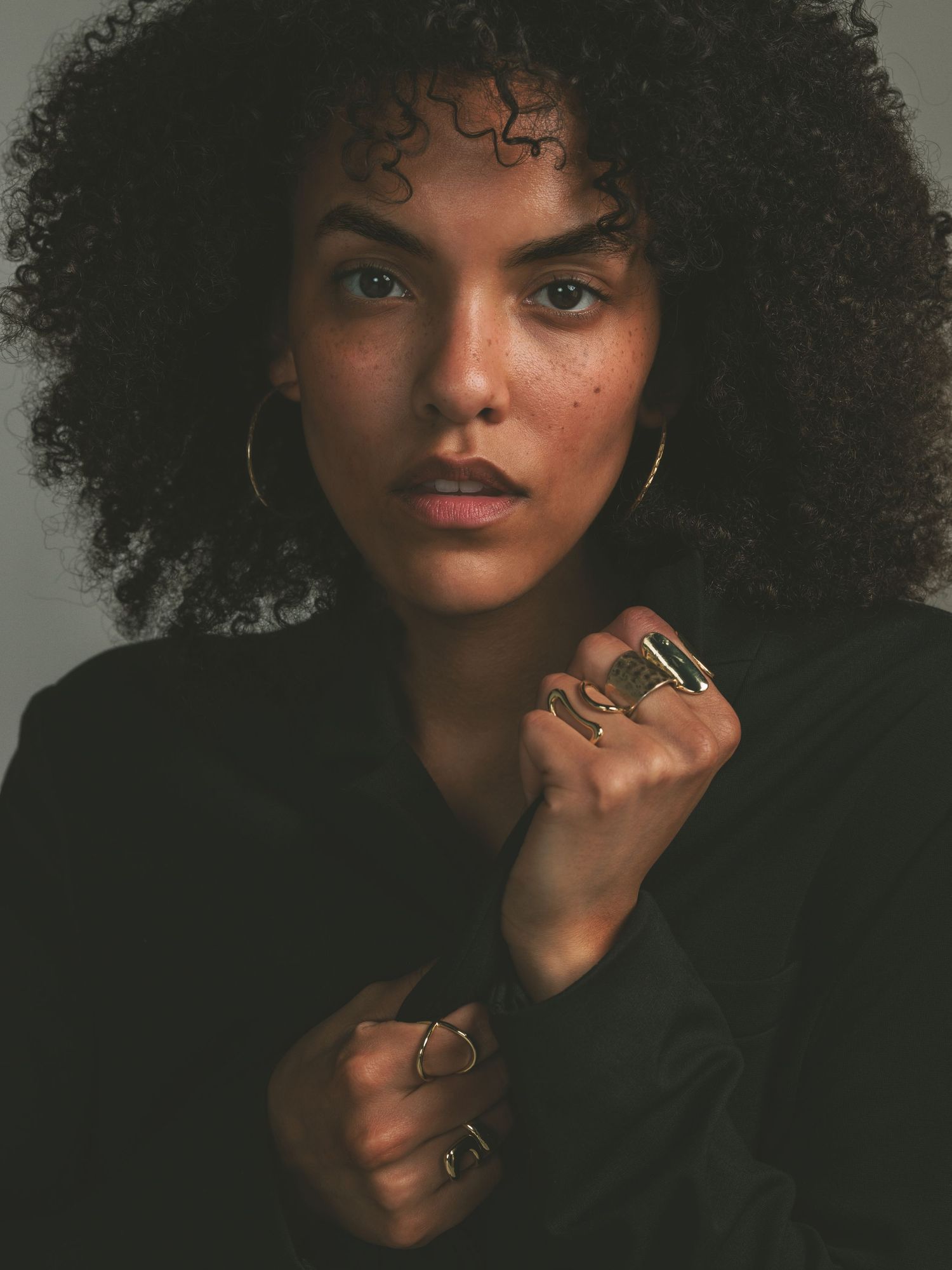 A series of five artistic portraits showcasing natural curly hair and delicate jewelry against a dark background.
