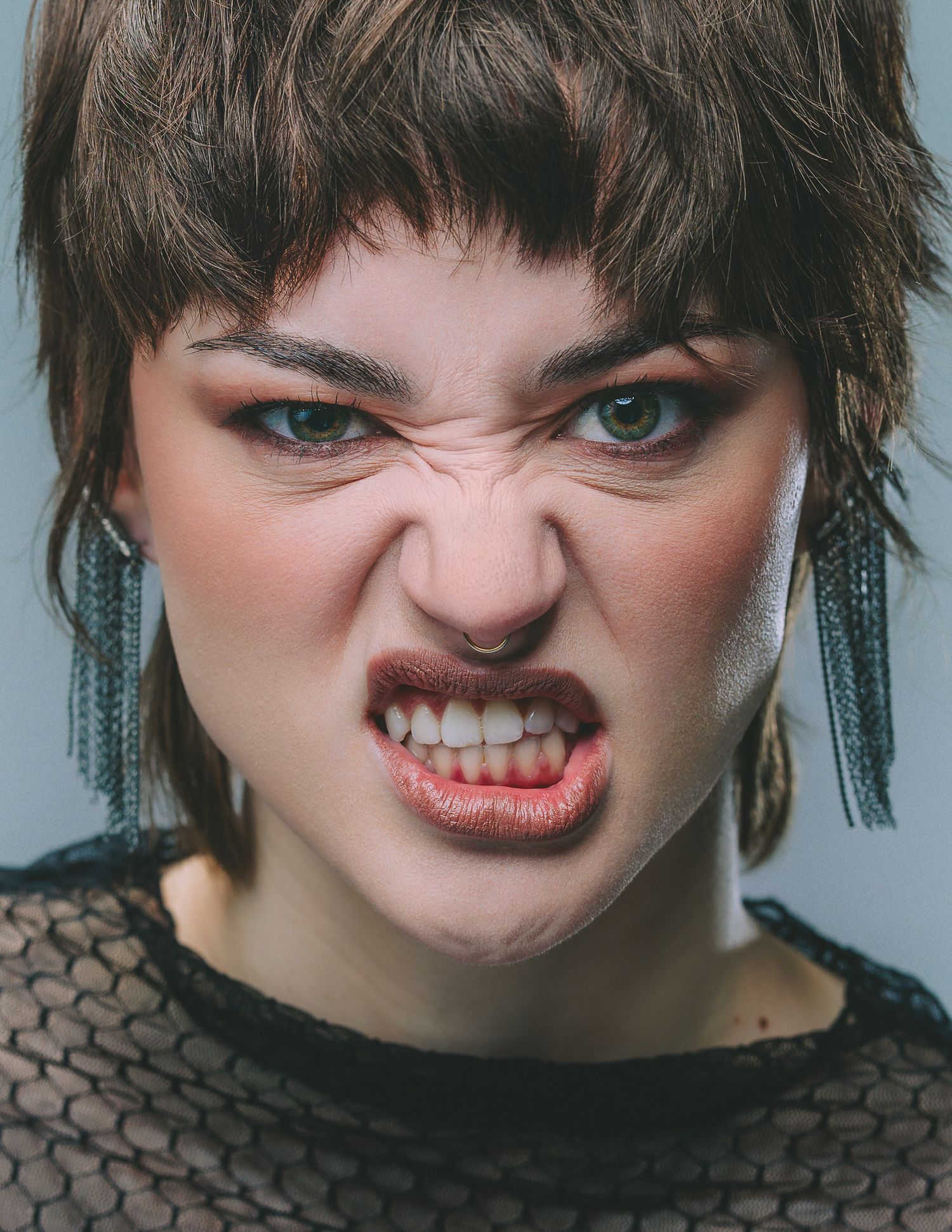 Close-up portrait of a young woman with short brown hair making an intense, snarling facial expression.