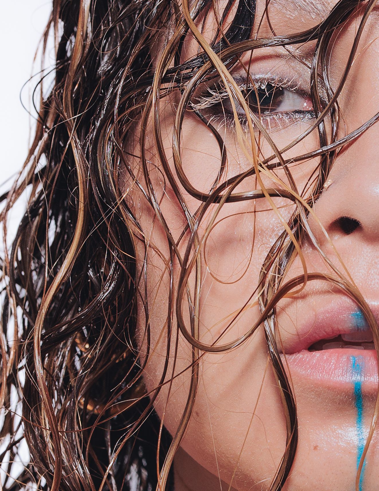 Close-up beauty portrait with wet tousled hair and dewy skin showing artistic makeup details.