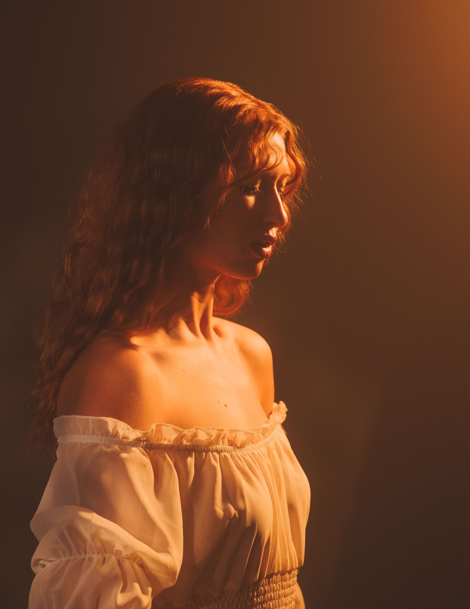 A person in a white off-shoulder top poses against a warm orange background in a romantic ethereal style.