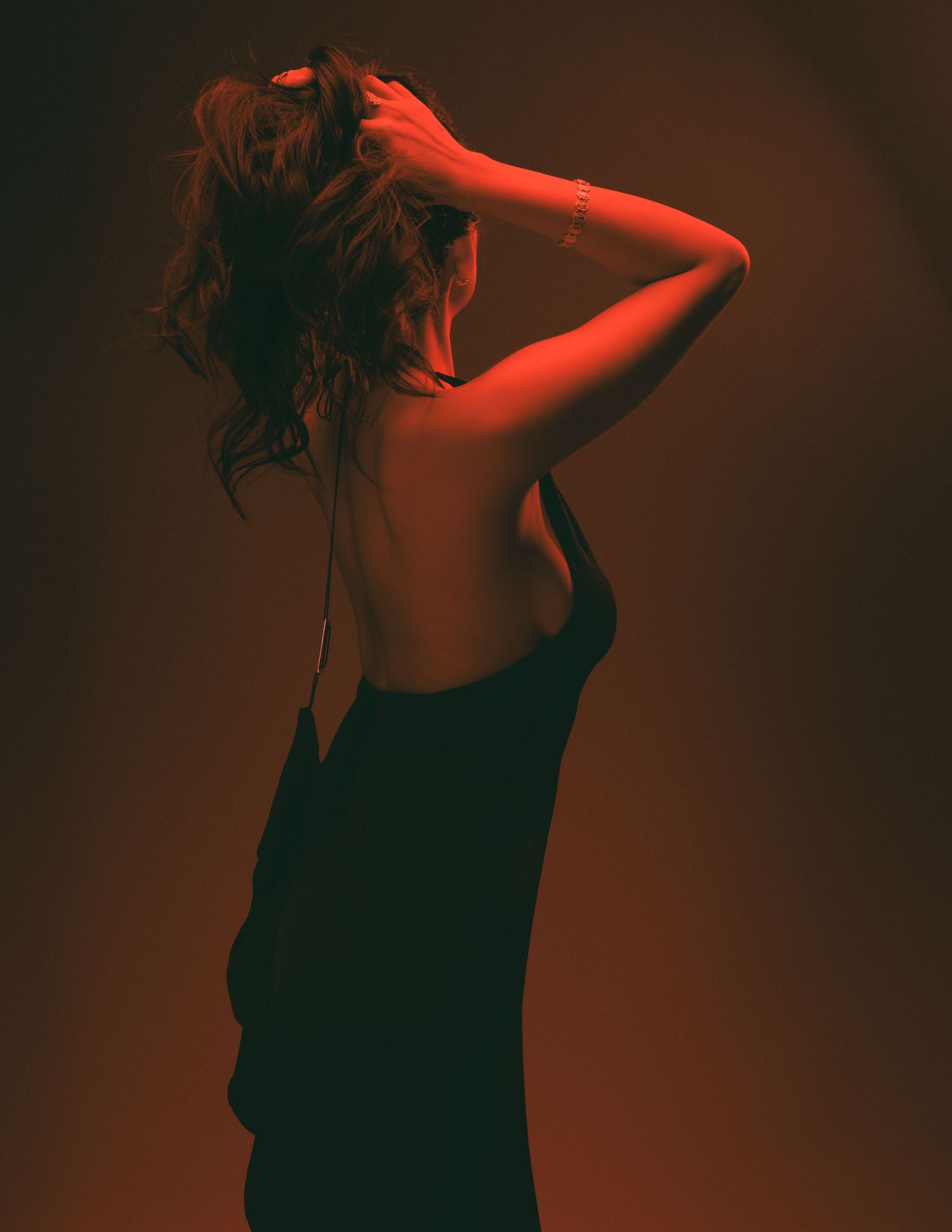 Silhouette of a figure in a black dress against dark background with dramatic red lighting.
