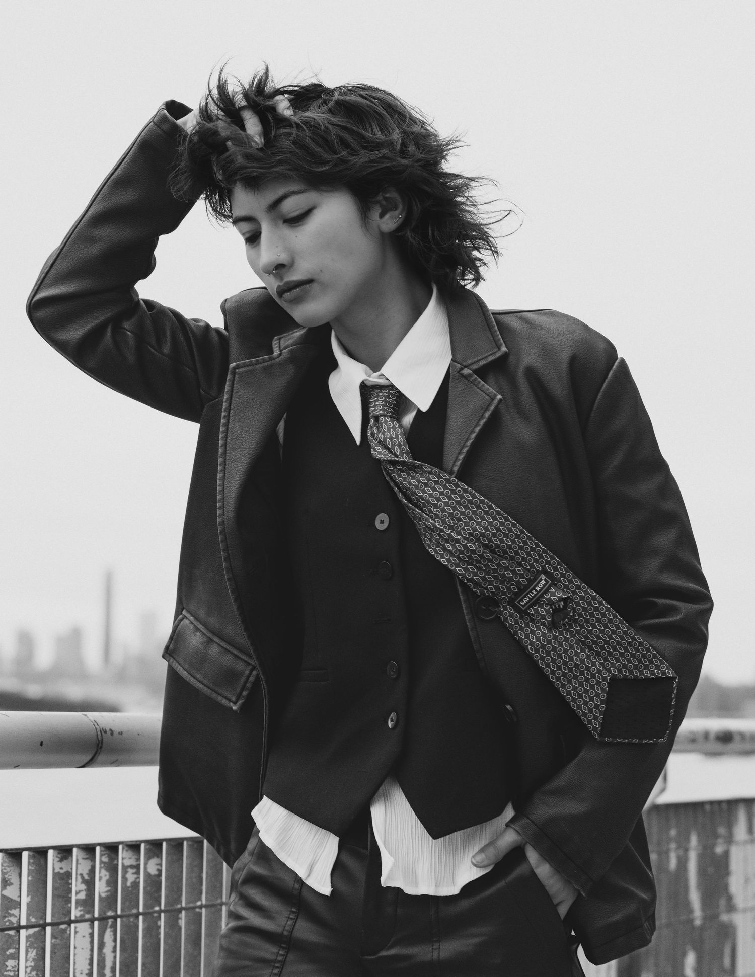 A series of black and white fashion photos showing a person in formal attire posing against an outdoor railing.
