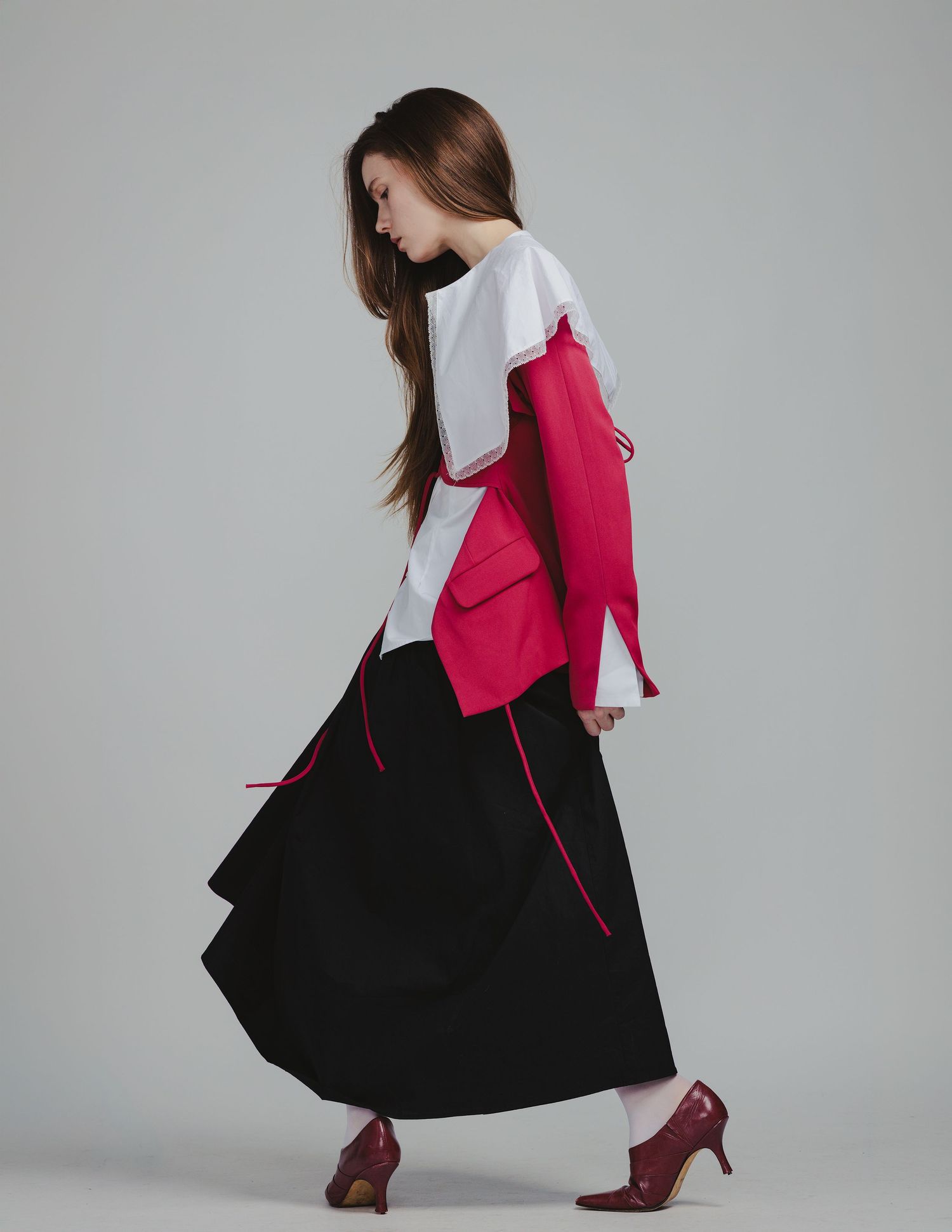 Model wearing red and white color-block jacket with black maxi skirt and burgundy heels in editorial fashion pose.
