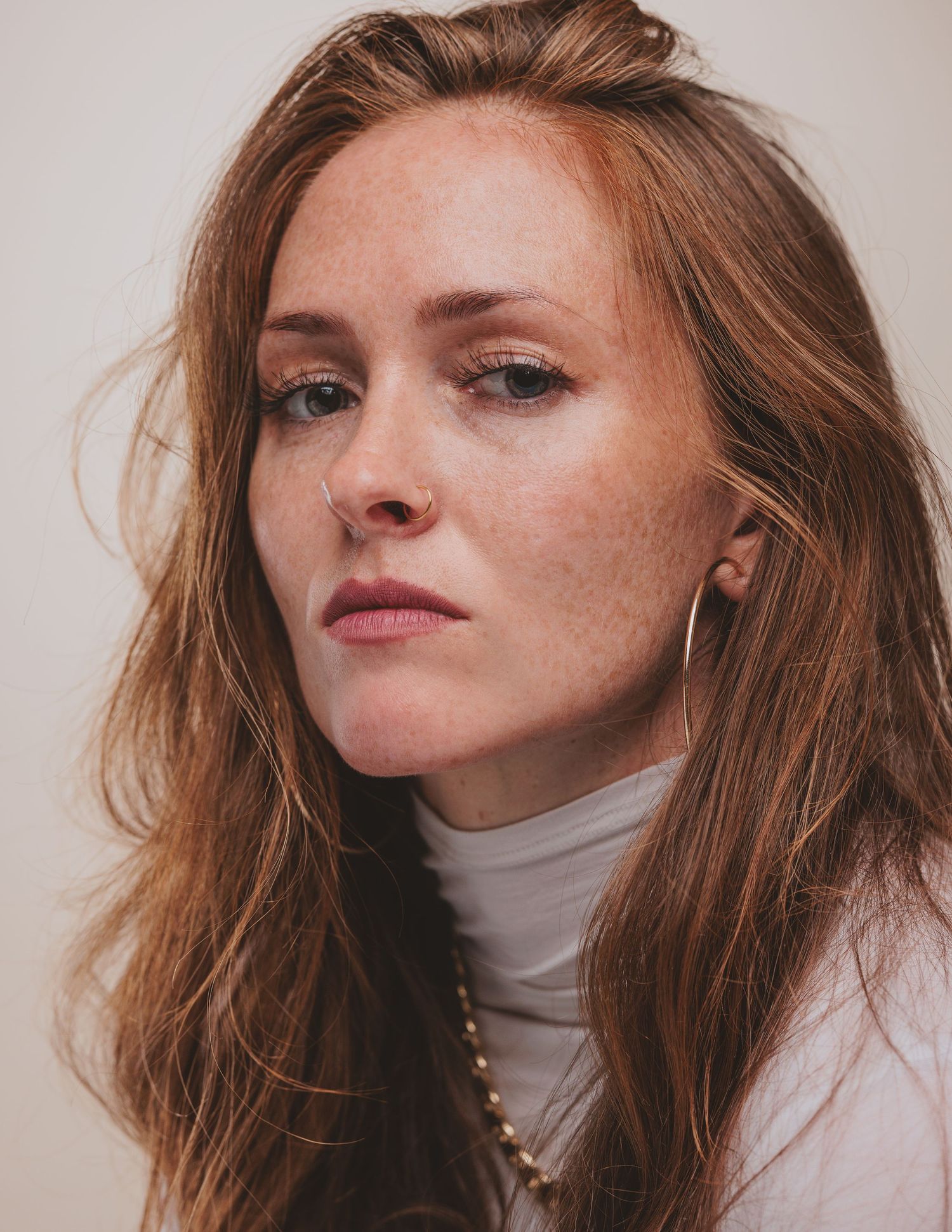 Person with red hair wearing a white turtleneck sweater poses against neutral background in artistic portrait series.