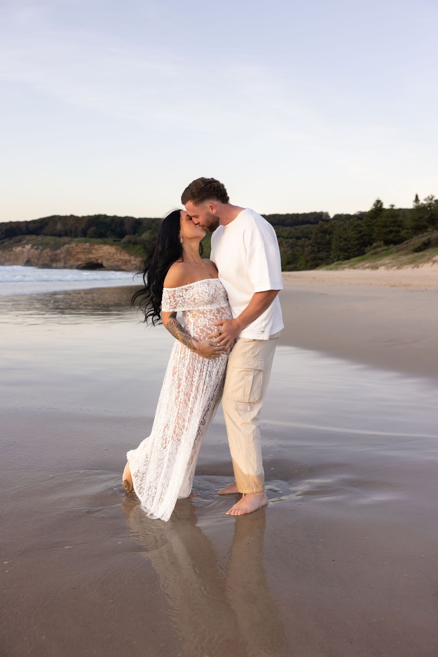 Expecting couple embracing at the beach.