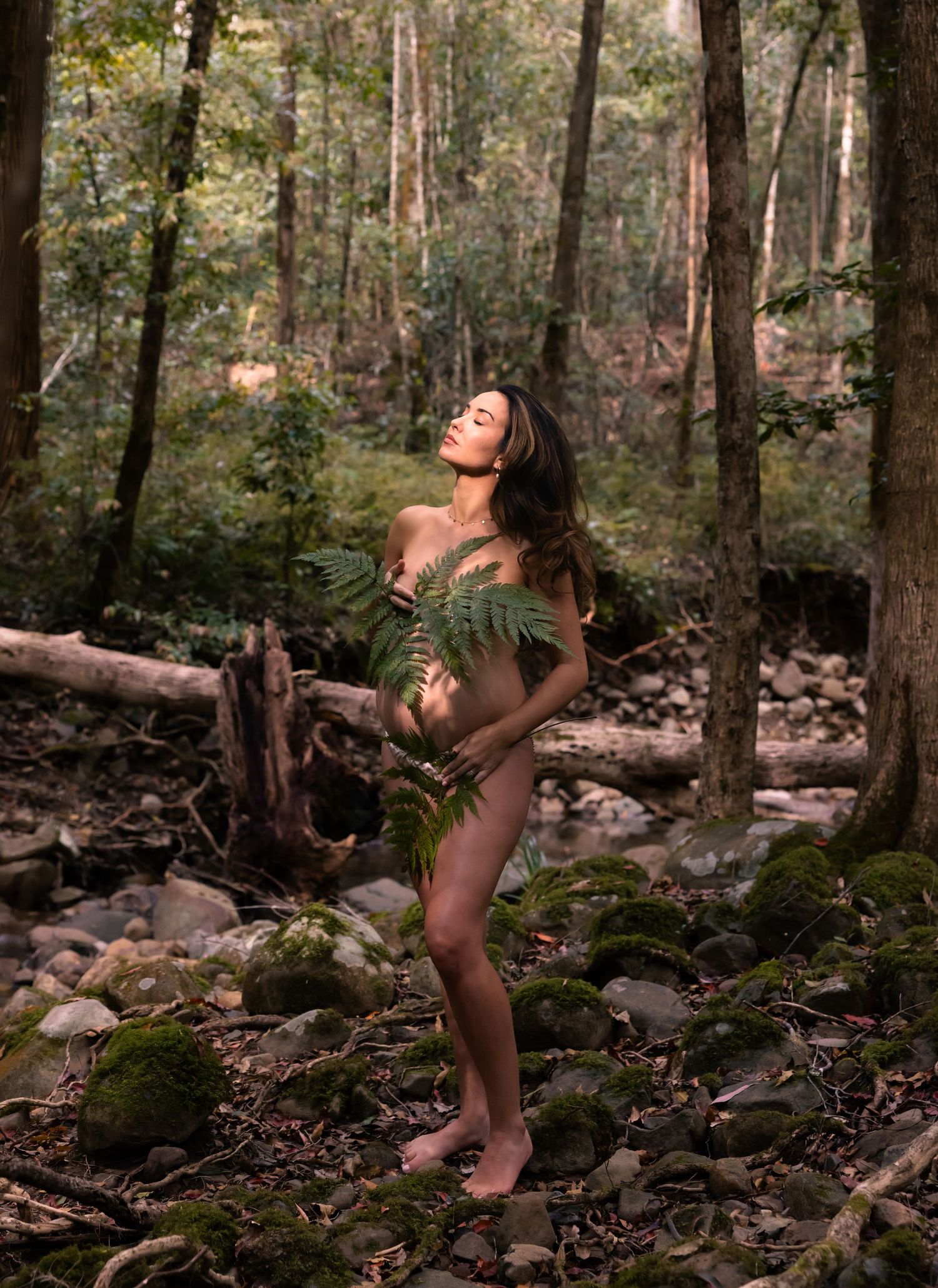 Woman tilts head to the sun in the bush at Glenrock with leaves and trees all around.