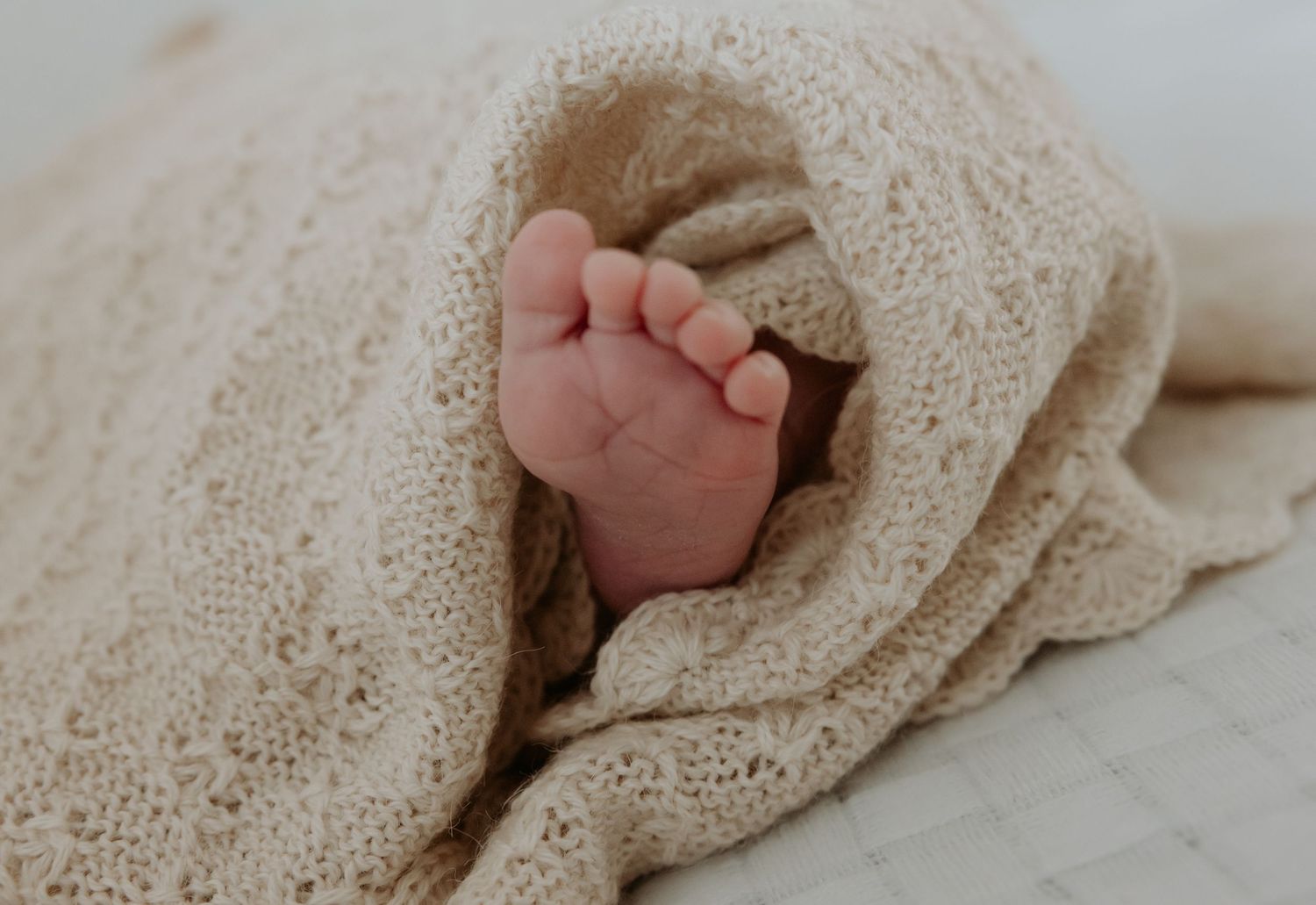 Close up of newborn babies foot surrounded by a warm cream knit baby blanket.