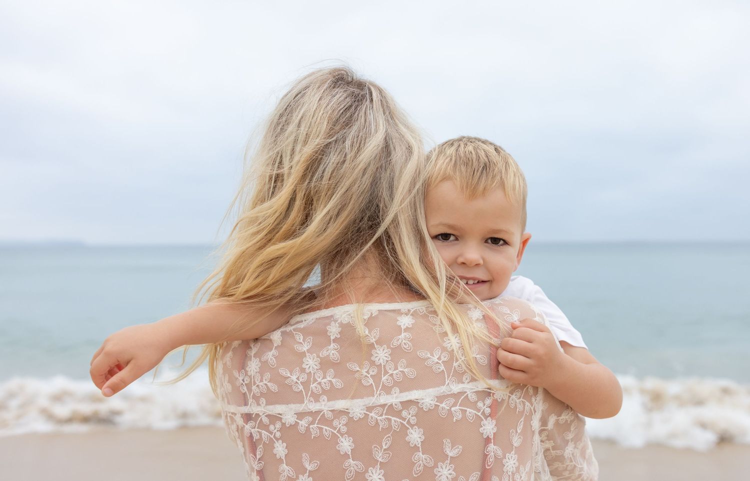 Boy peaks out from behind his mother's hair with a big smile on his face in Newcastle.