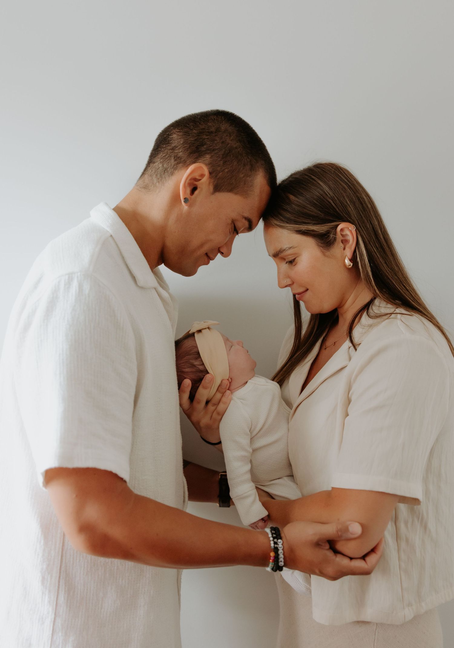 Mother and father lean in towards each other, heads resting both looking at their newborn baby girl.