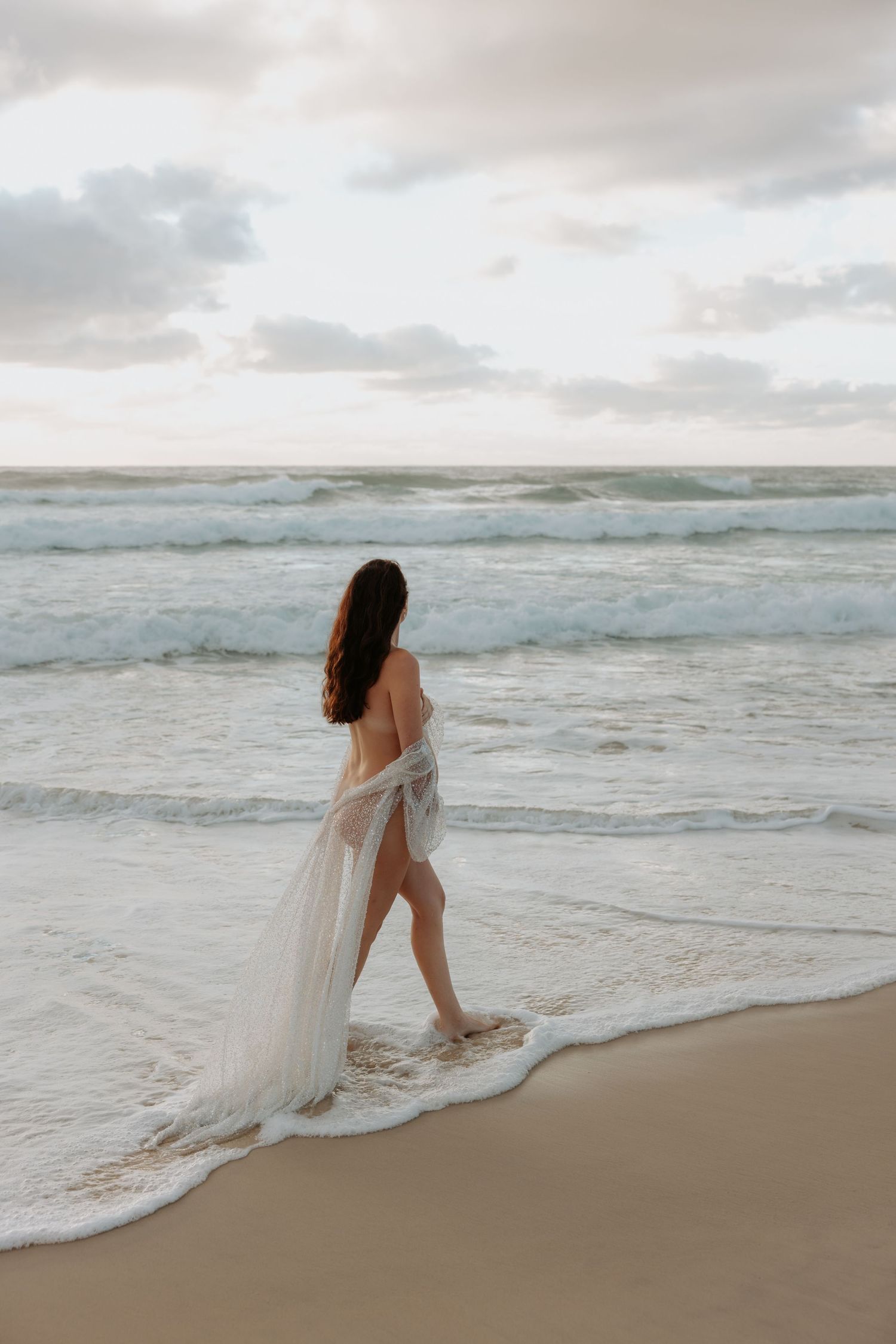 Romantic imagery showing a woman calmly walking in the shallow waters by the oceans edge.