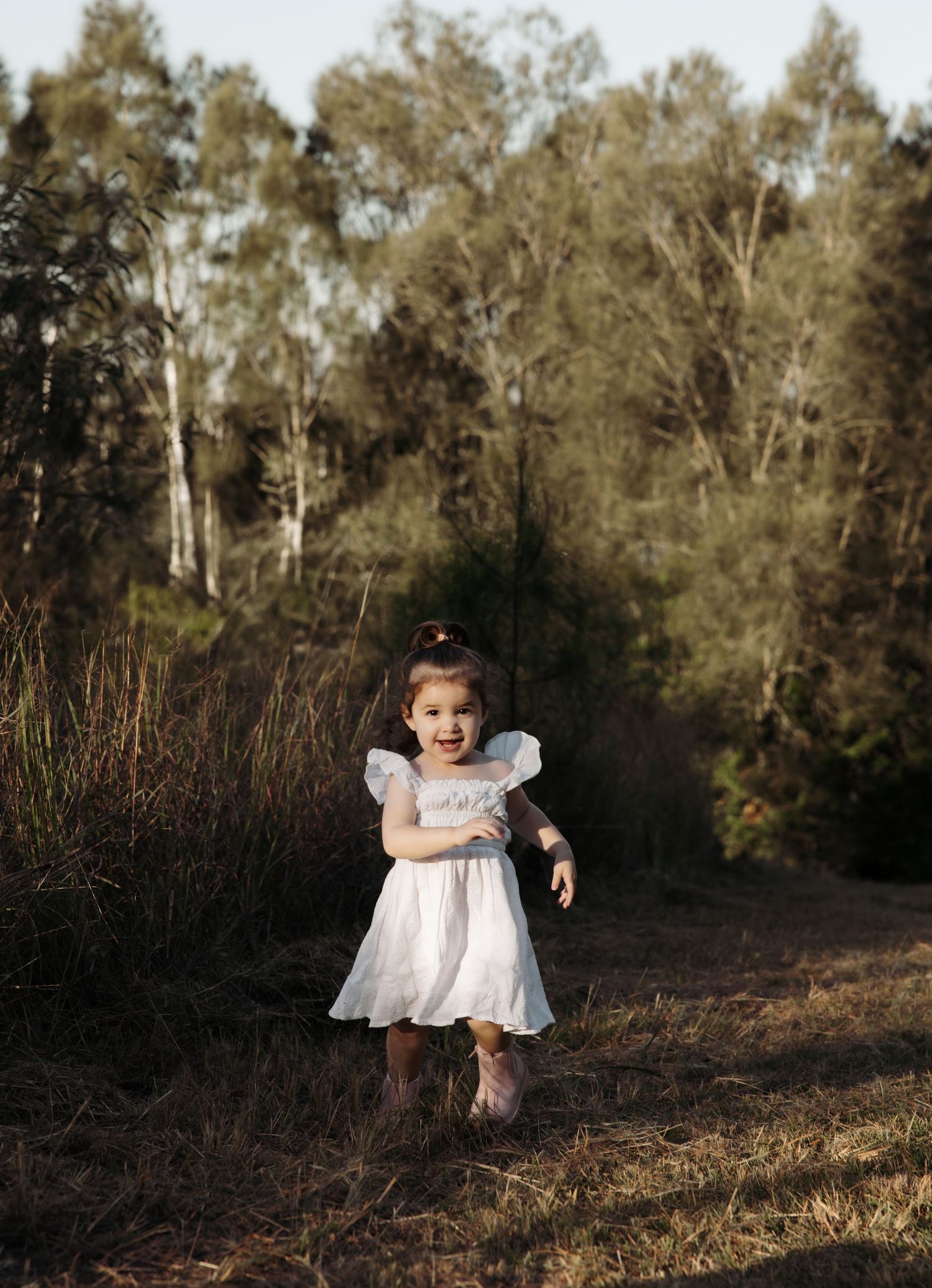 Girl running up a garden pathway, tall tress behind her, a huge smile on her face.