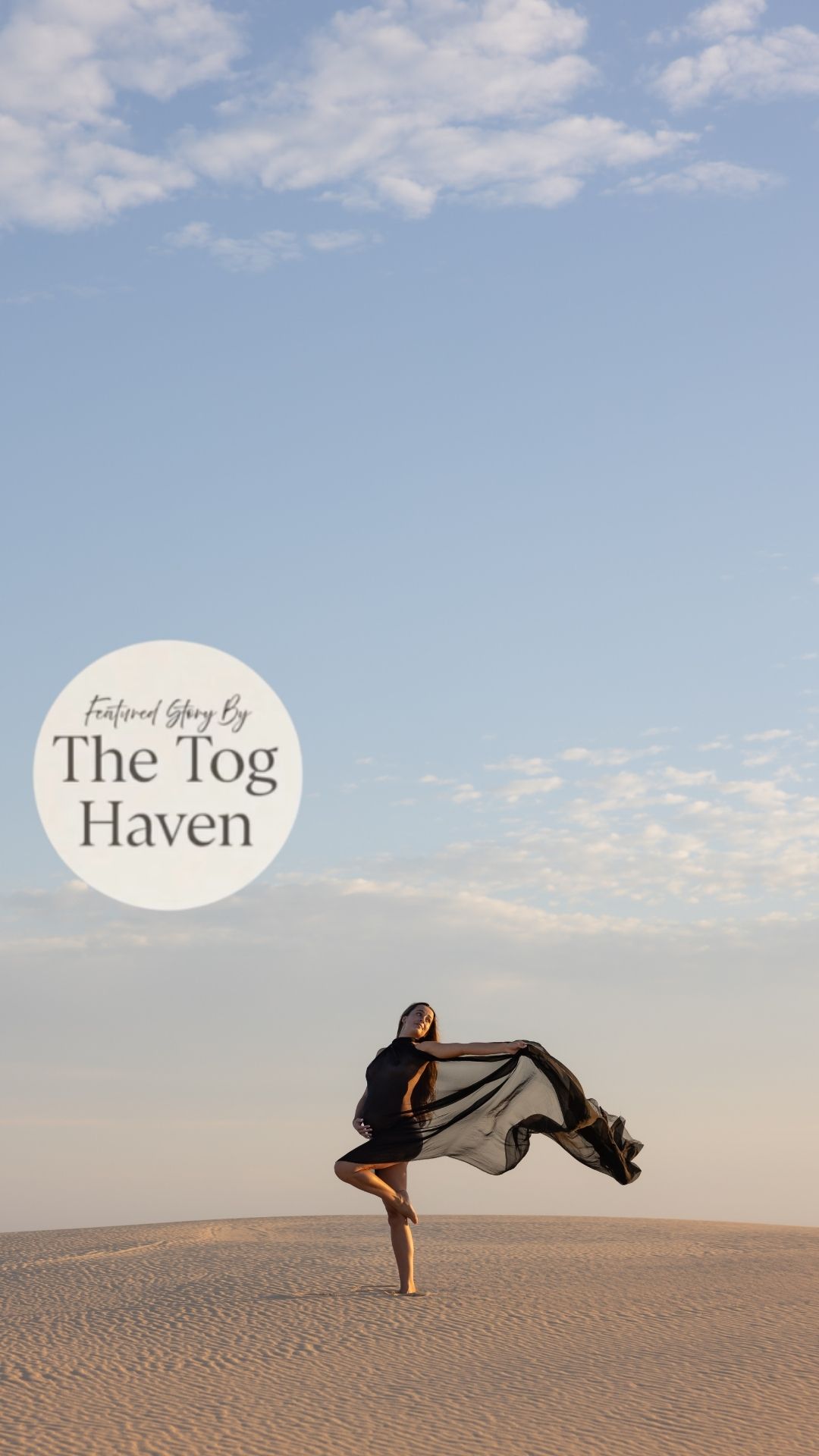Woman standing in flowing black fabric at the sand dunes holding her pregnant belly. Negative space of the sky shows how vast the area is.