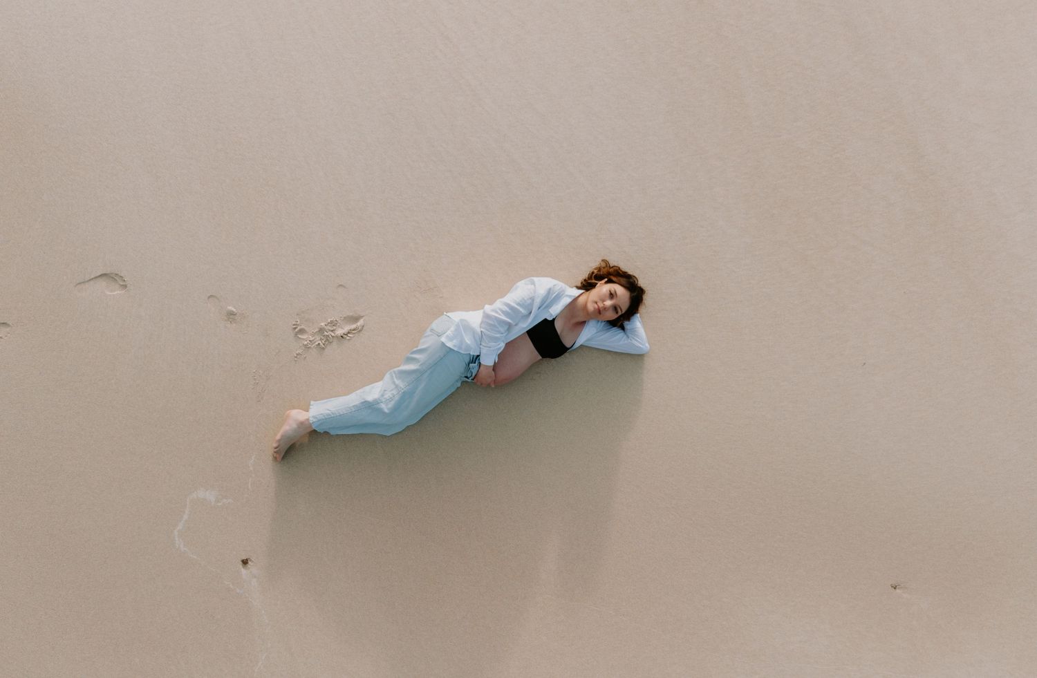 Pregnant mother lays on the sand at Newcastle Beach and looks up at the drone.