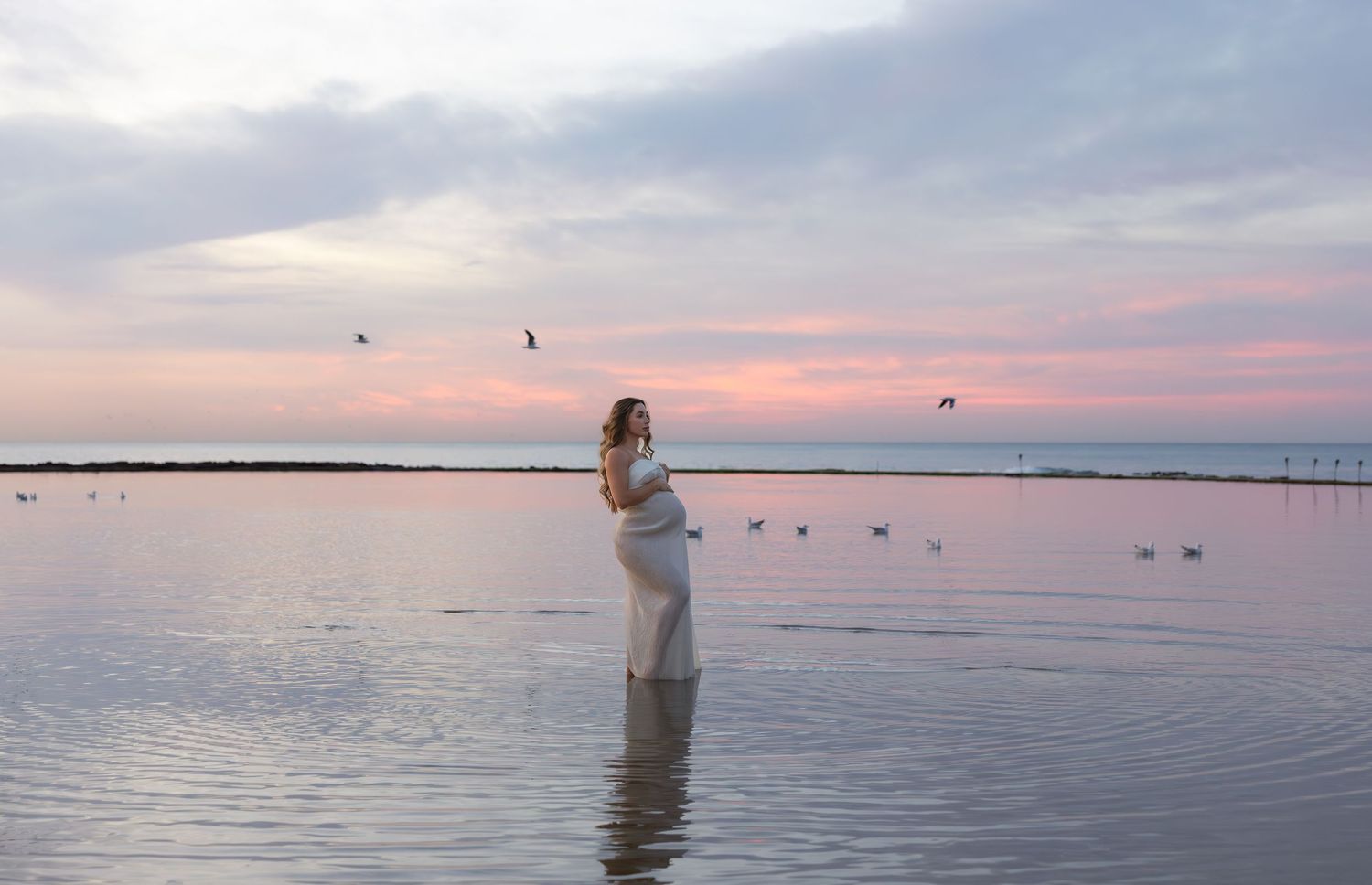 Pregnant mother at Newcastle Baths with seagulls drifting on the water near her.
