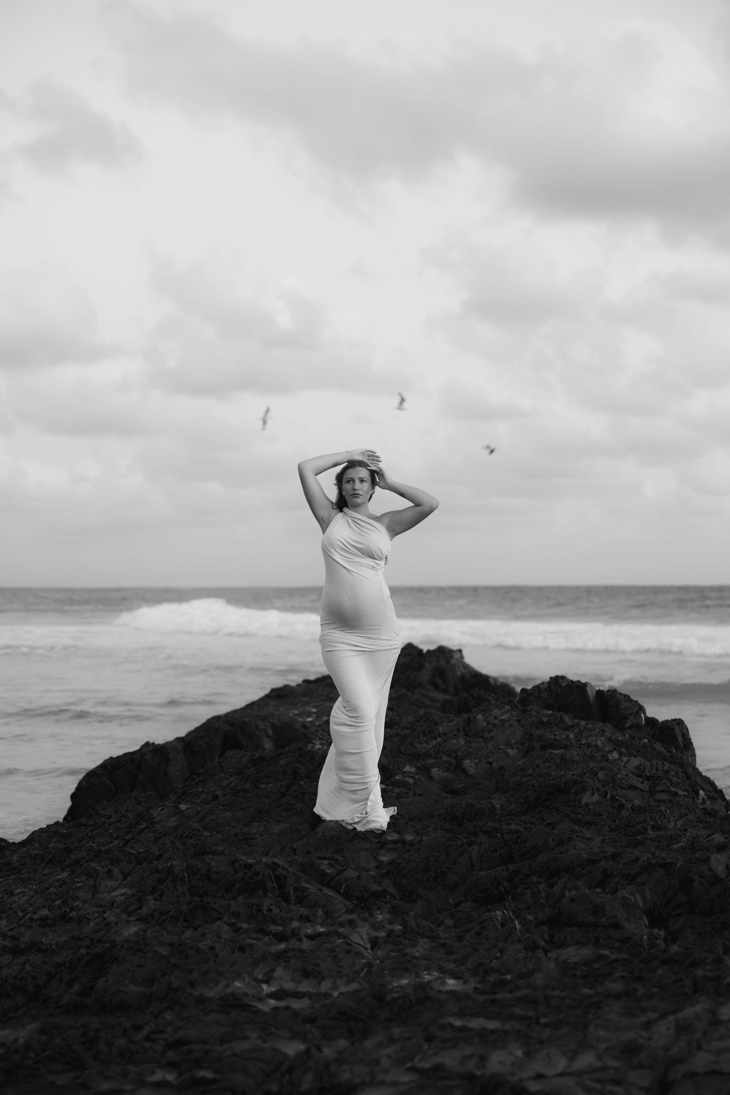 Woman stretches her hands above her head as birds fly above her signifying the new life she is carrying.