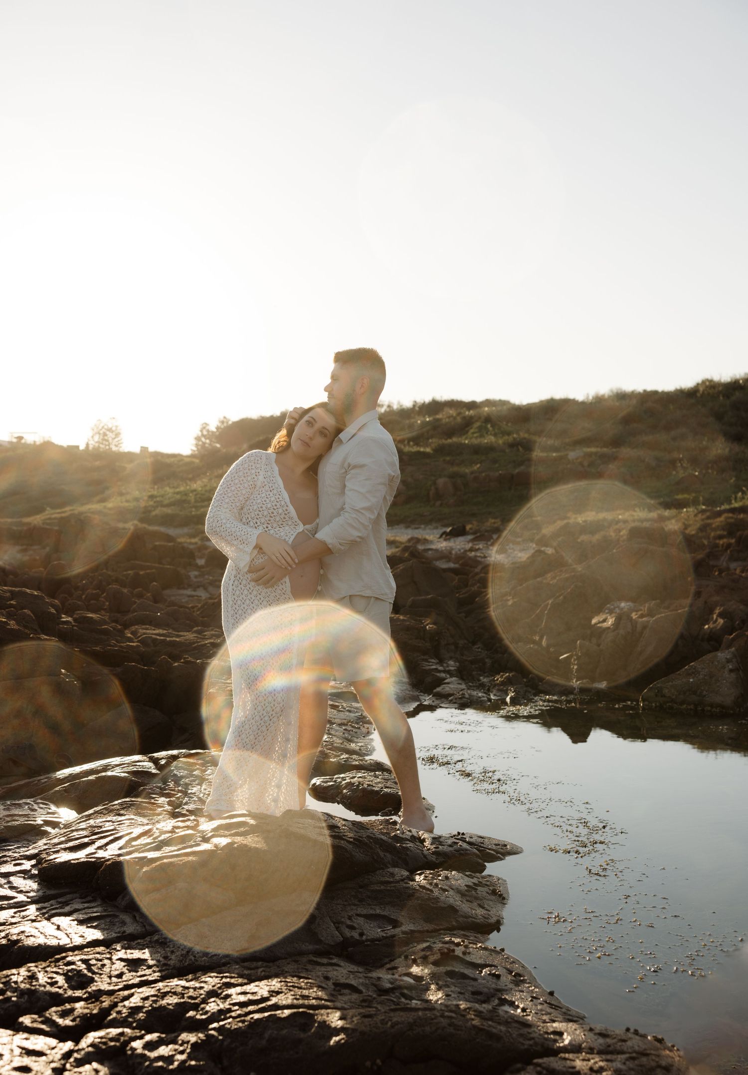Water droplets frame the subject, a maternity couple cuddling near the rocks at a Port Stephens beach.