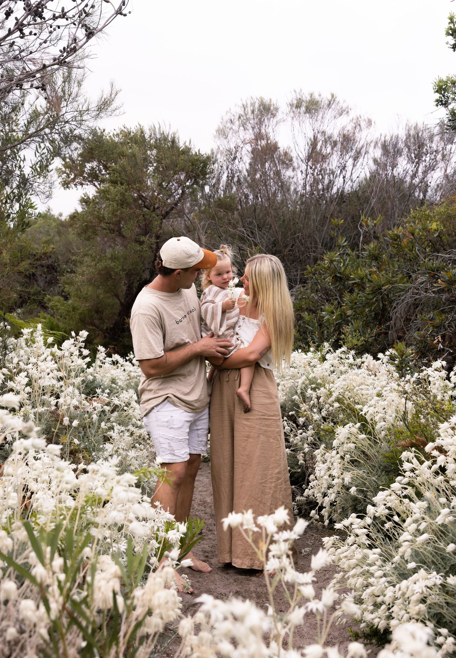 Mother and father hold daughter above hundreds of white wild flannel flowers on the Central Coast.