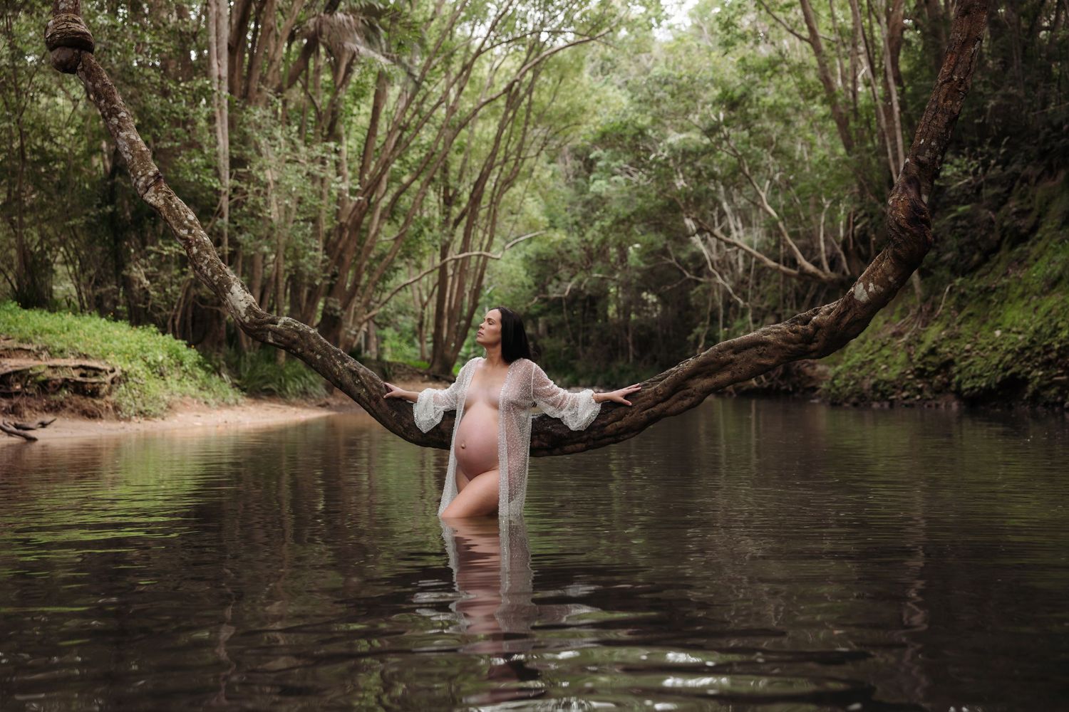 Pregnant mum wearing sparkle robe in Glenrock Lagoon surrounded by green trees and hanging branches.