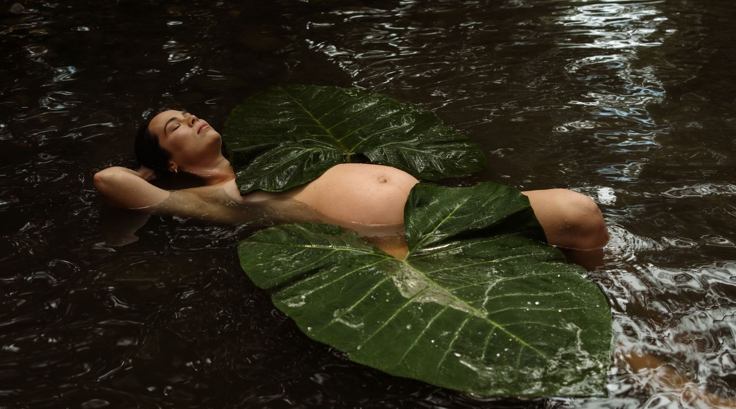 Adventurous mother lays in creek water with huge plant leaves resting onto of her.