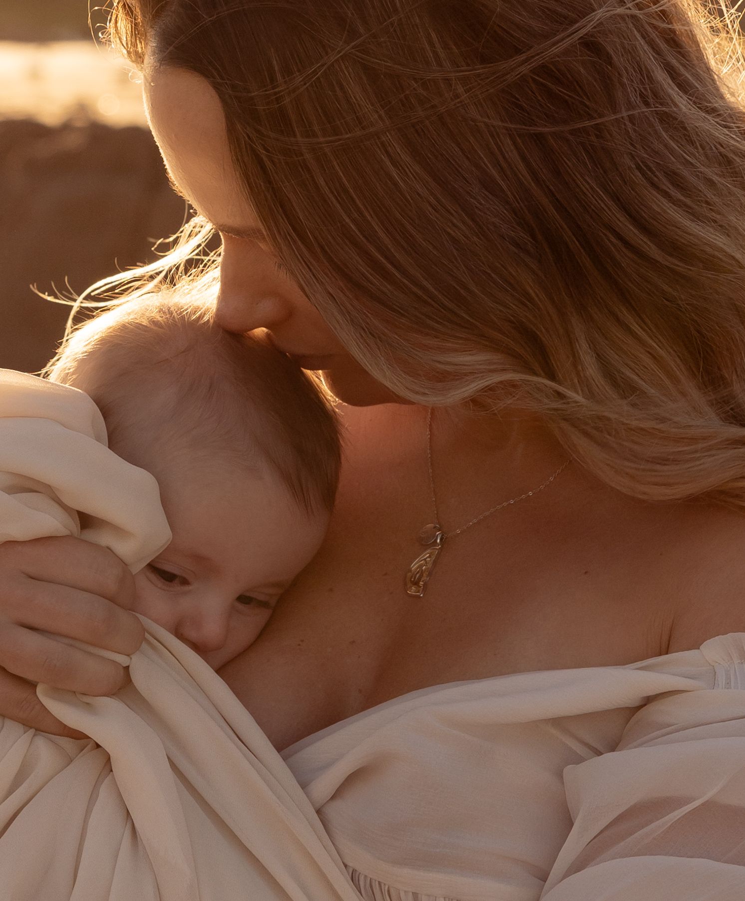 a cropped close up of mother and child glowing in golden light. The mother gently kisses her baby on her head.