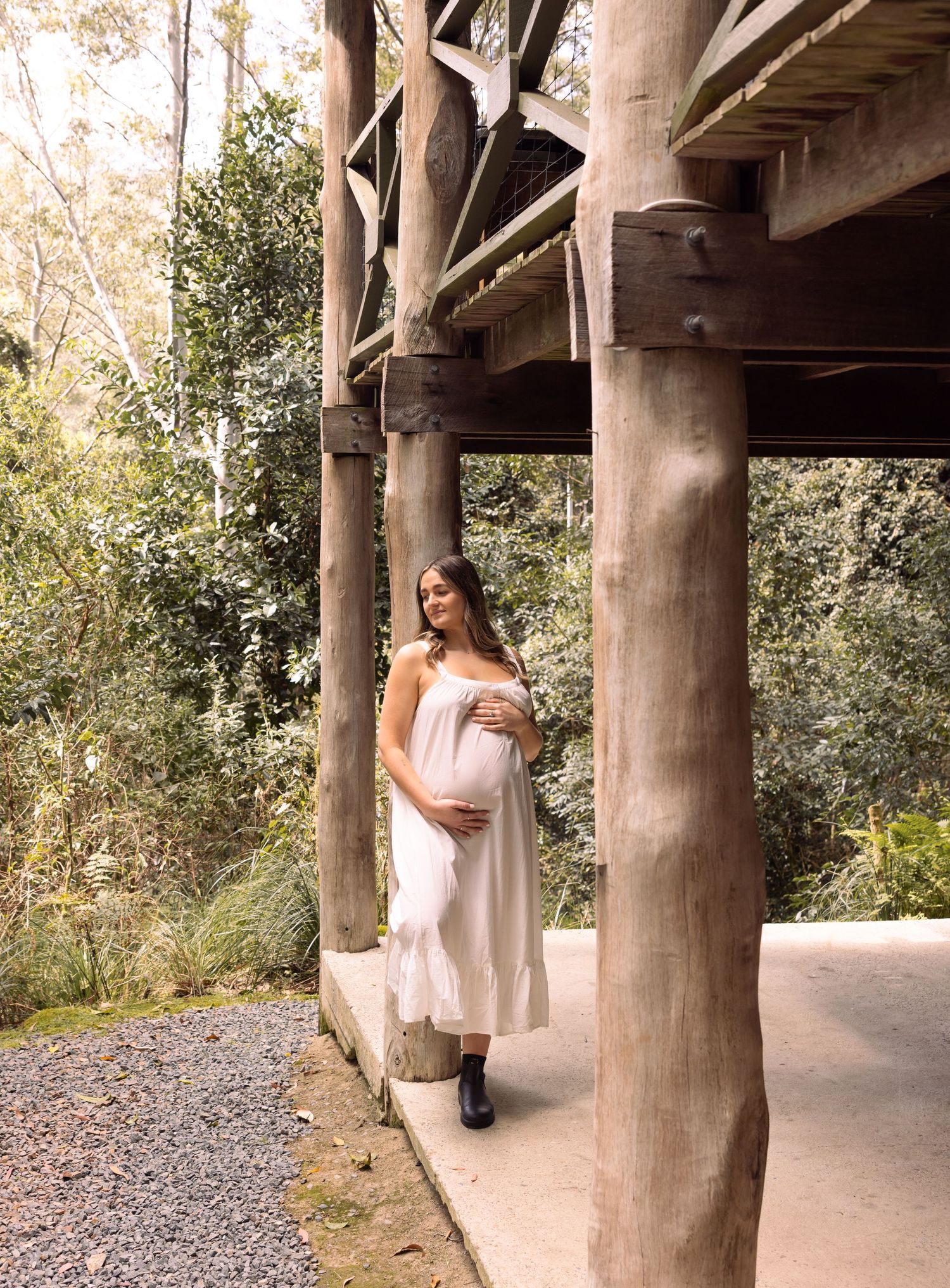 Pregnant mother leans resting against a timber cabin while on a babymoon holiday.