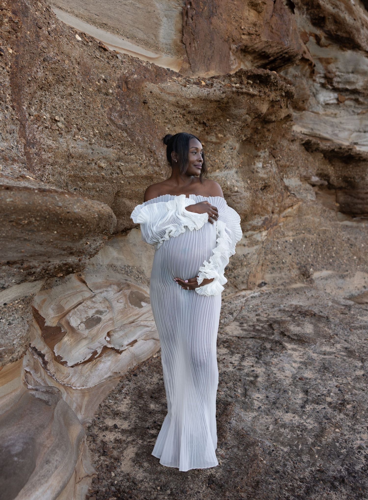 Woman holds pregnant belly and looks out over the rock formations.
