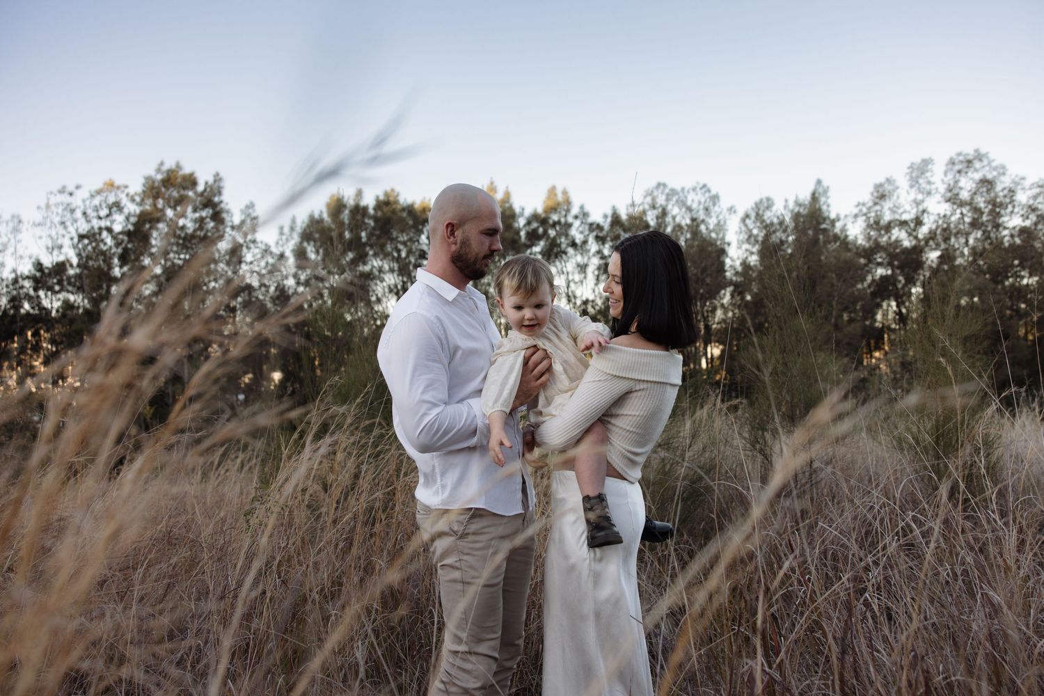 Man and woman holding their child between them in the long grass in Lake Macquarie.
