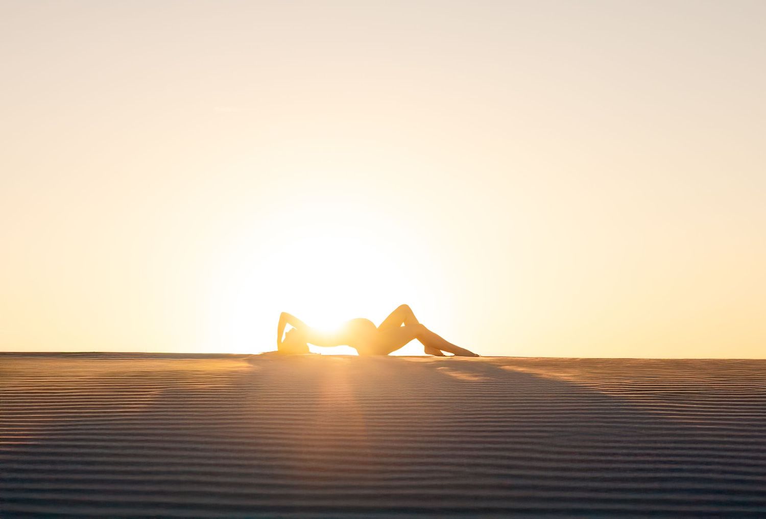 Woman lays in the rippled sand dunes at Port Stephens with the sunset behind her making her glow.