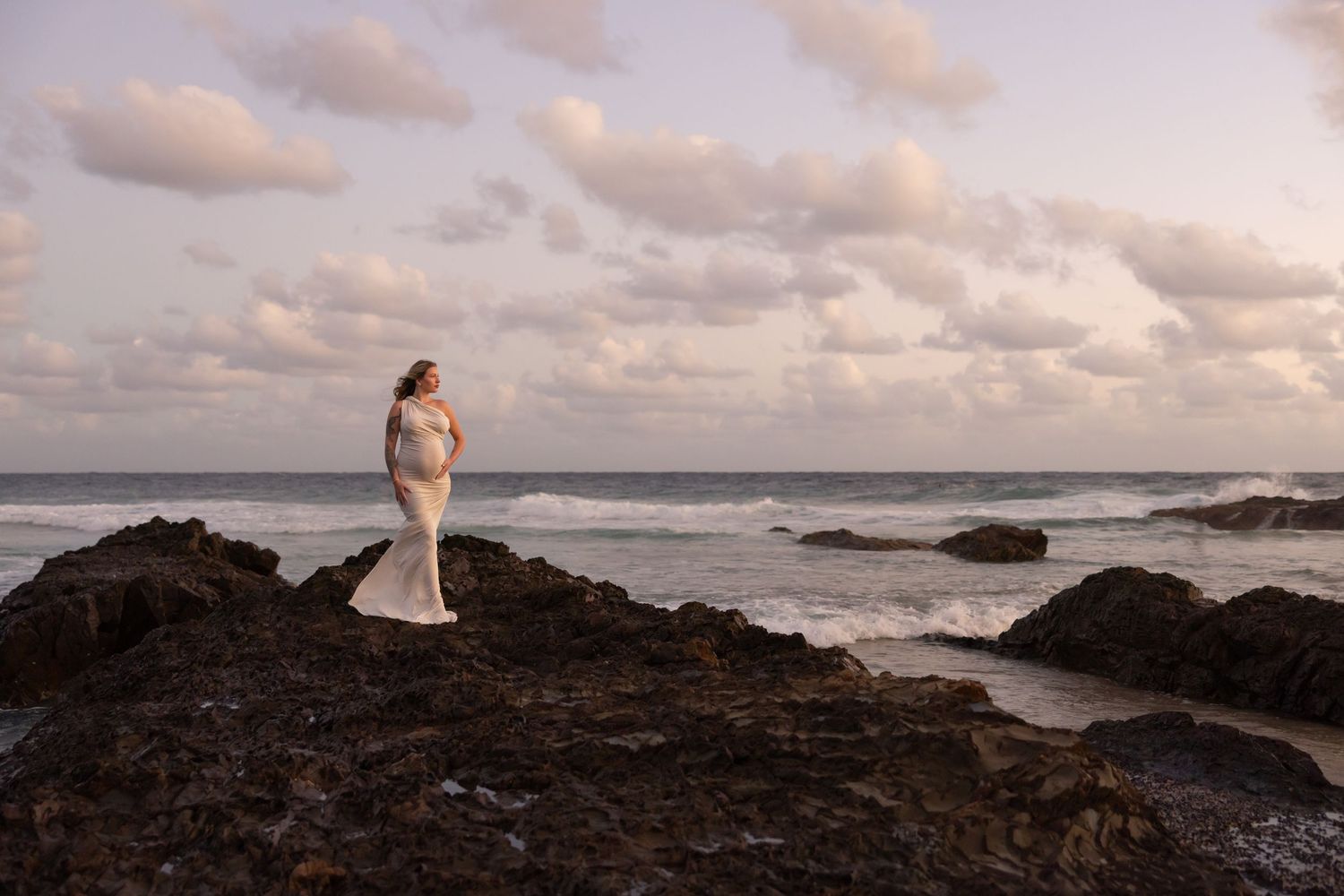 Woman stands on the seemingly endless rocks that jut out above the ocean at sunrise.
