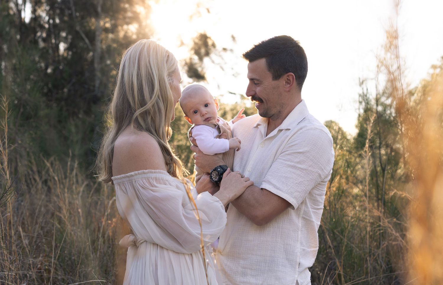 Mum and dad framing baby for a family photoshoot with the golden sunlight streaming in behind them.