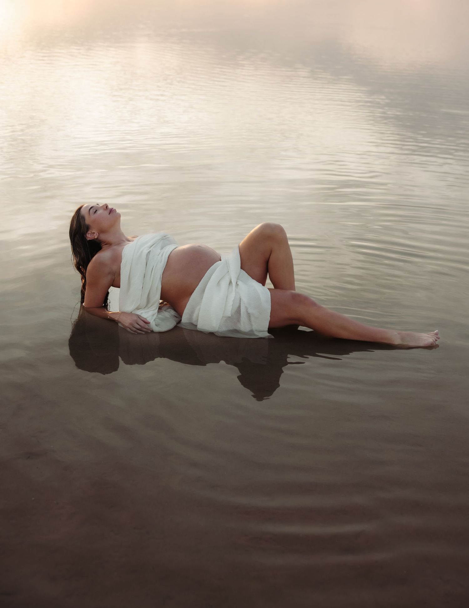 Expecting mother in the shallow calm waters leaning on her elbows.