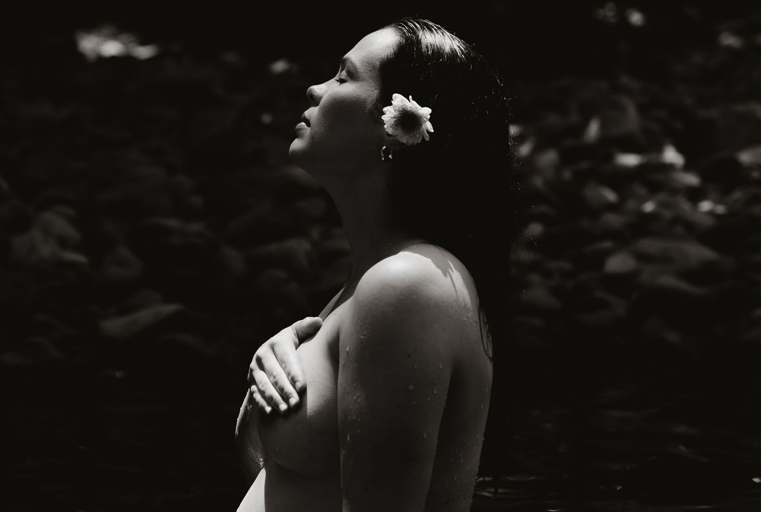 Portrait of a pilates instructor standing in a shallow creek with a flower in her hair during a peaceful outdoor session.