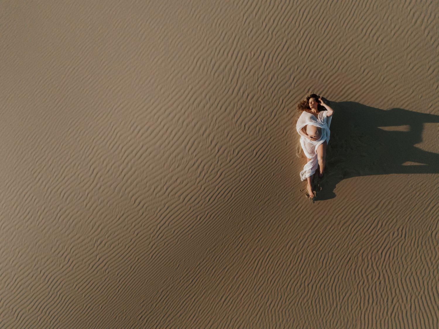 Aerial drone image of a maternity mum lying on patterned sand dunes in Newcastle.