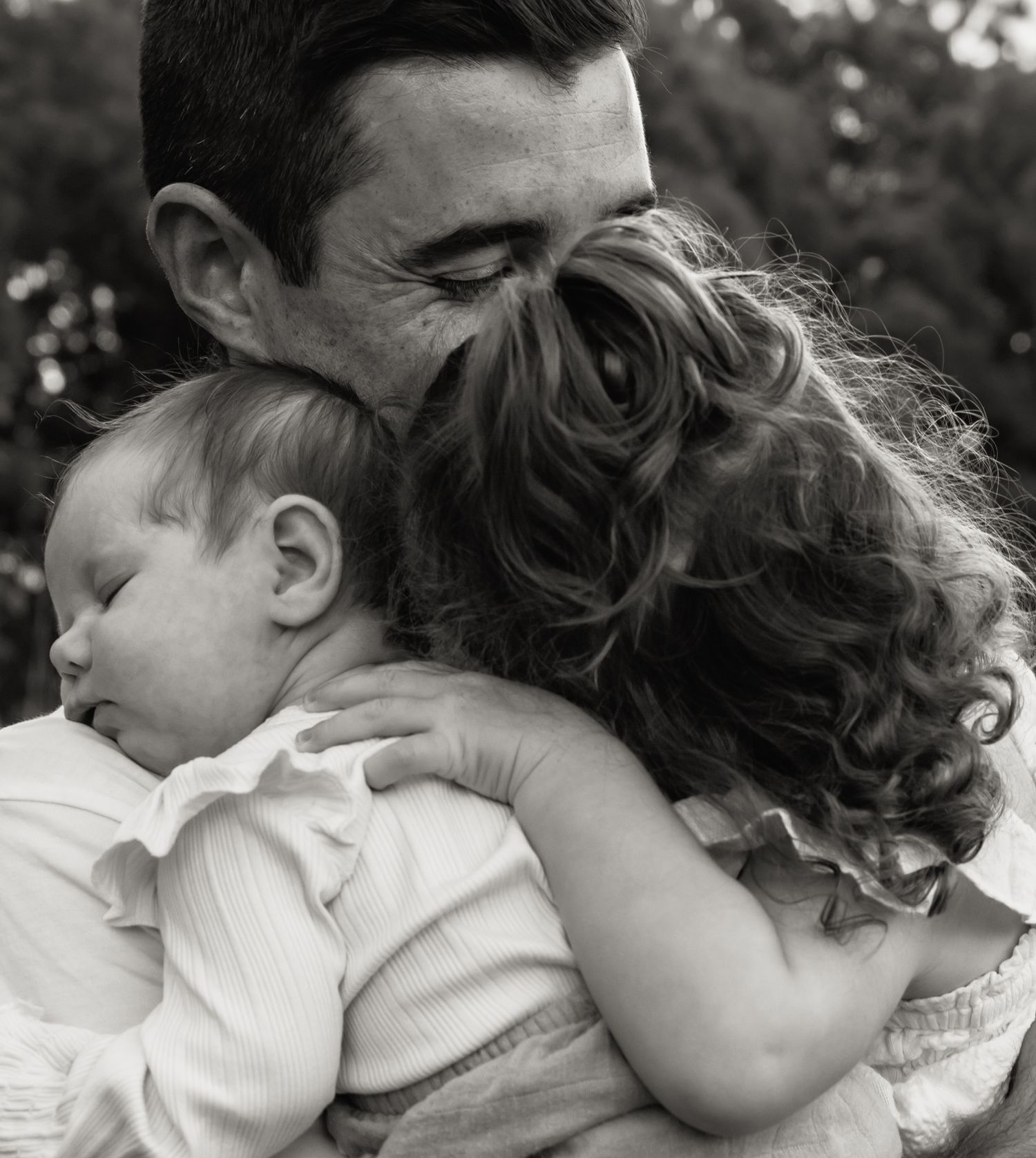 Father holds both of his daughters close, smiling and enjoying the moment, happy with this life they have created.
