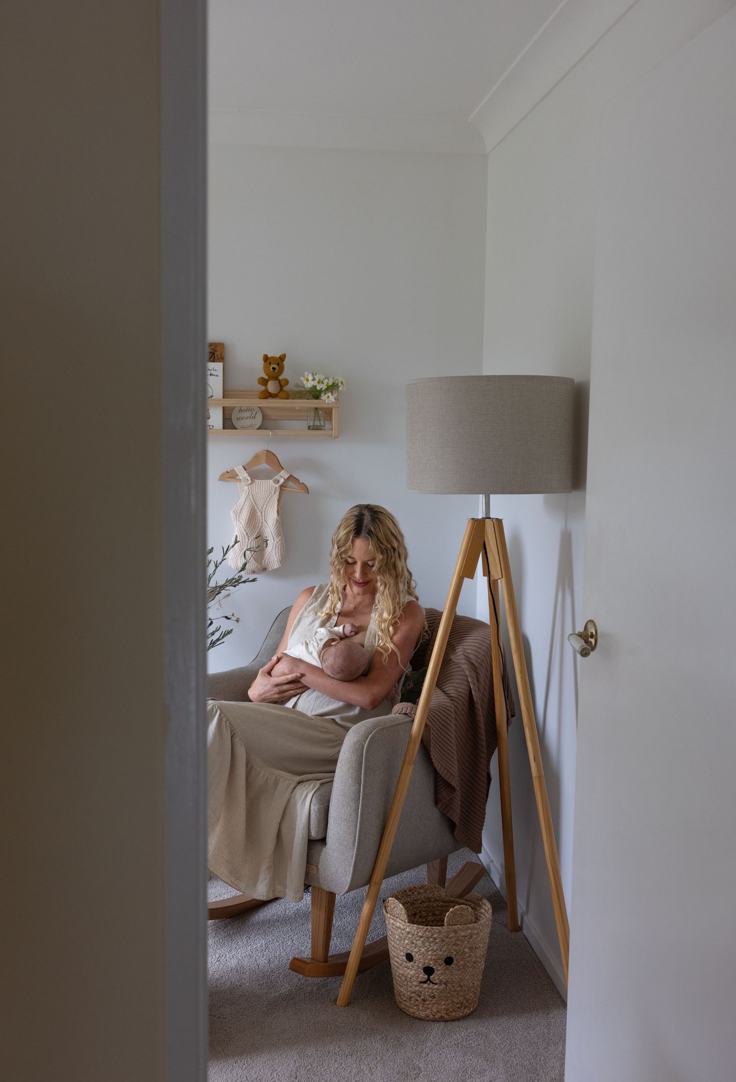 New mother rocking her newborn baby while feeding him to sleep pictured in the nursery with house plants, soft toys and baby books.
