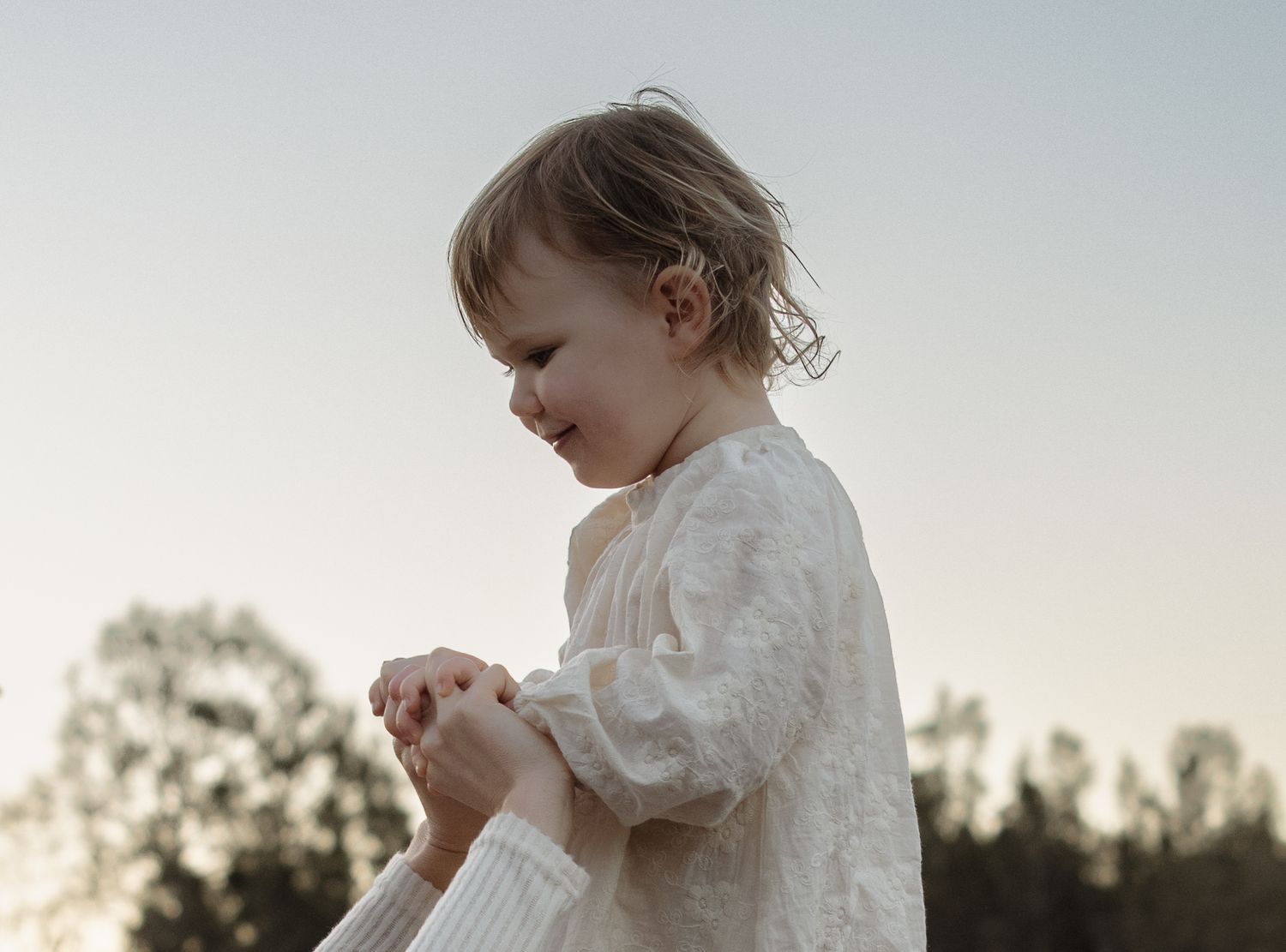 Child sits high on her fathers shoulders, holding her mothers hands at blue hour.