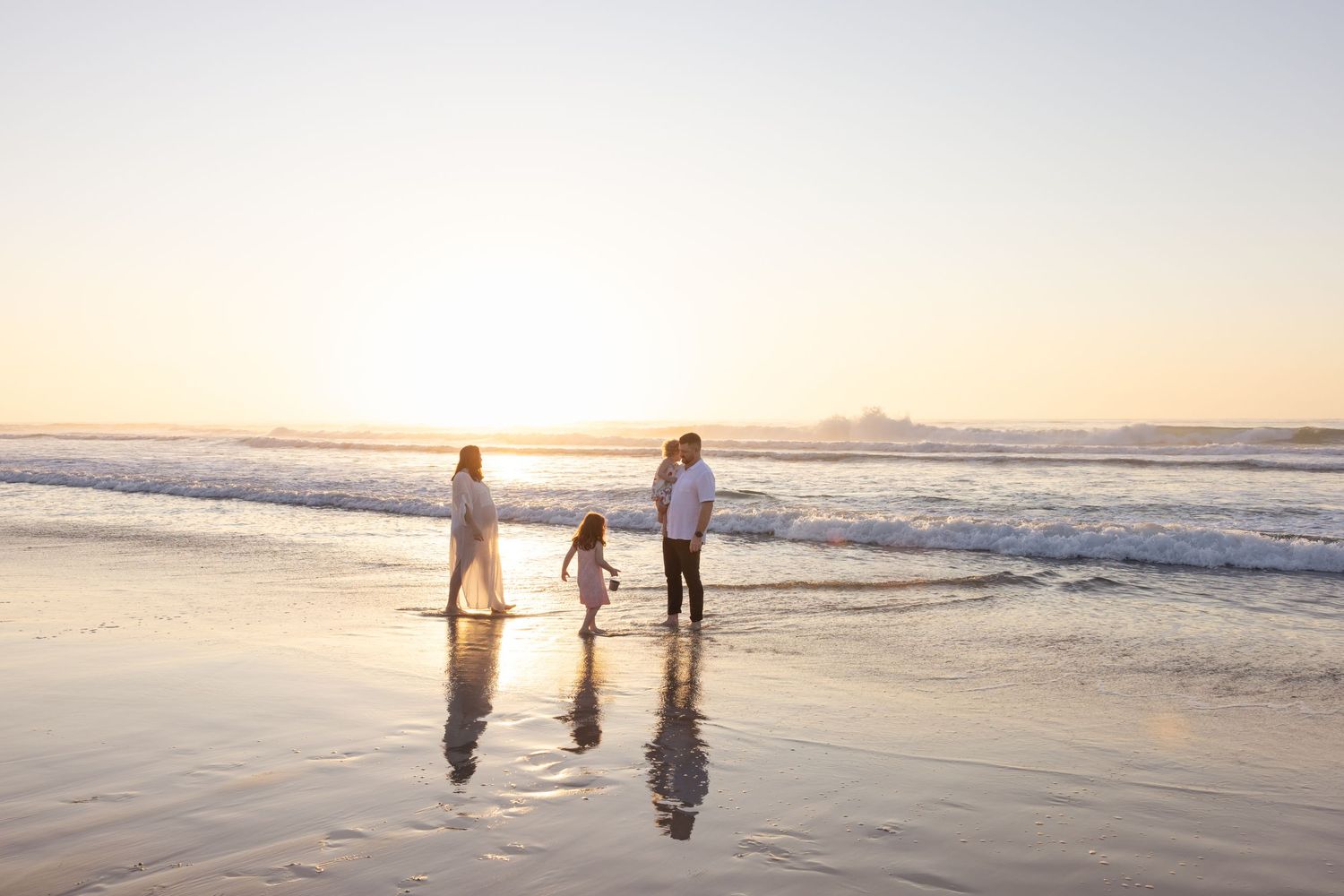 Family walking together through the shallow ocean water at golden hour at Caves Beach.