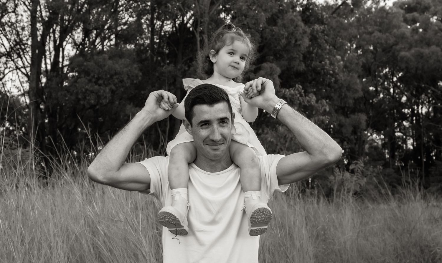 Dad carries daughter on his shoulders. Dad has a big smile on his face.