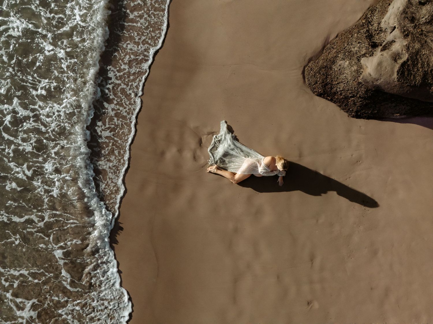 Maternity mother laying on the sand as the gently waves roll up the beach.