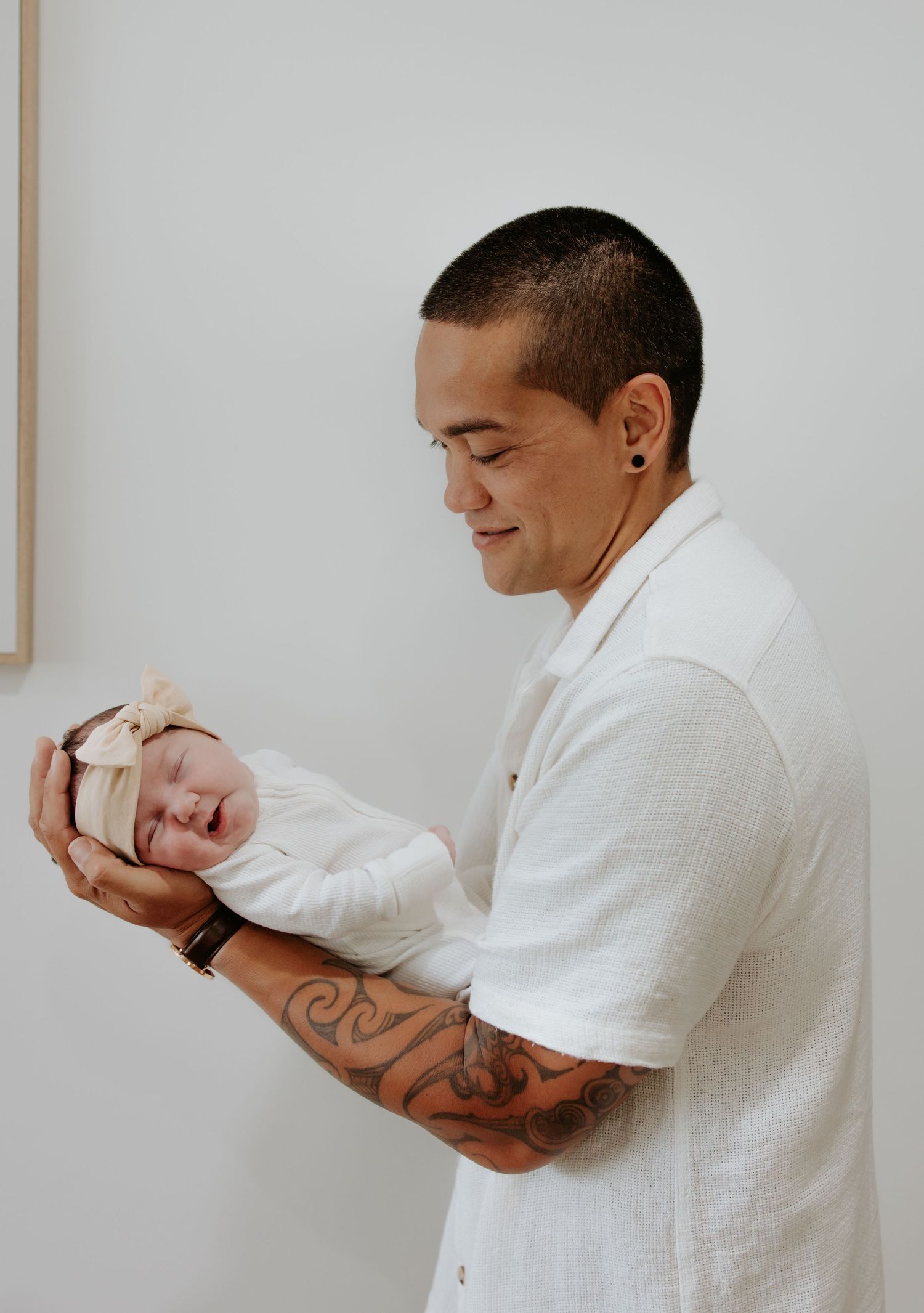 Dad holds baby daughter in tattooed arm as baby girl smiles and turns head towards the camera. Taken at home.