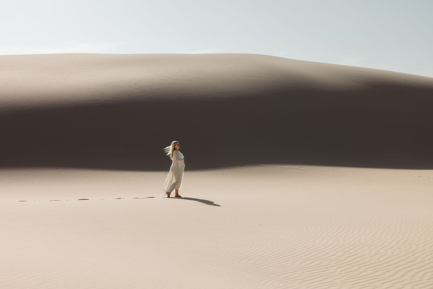 Woman in front of a large sand dune in Port Stephens. The shadow of the sand dune illuminates the mother who is in the full sun.