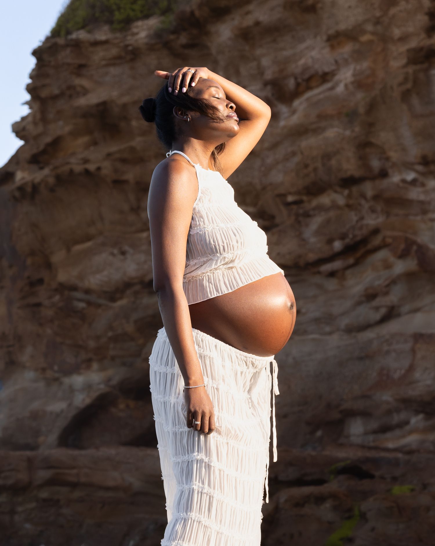 Pregnant mum sweeps hair from her face while enjoying the warm summer sunshine.