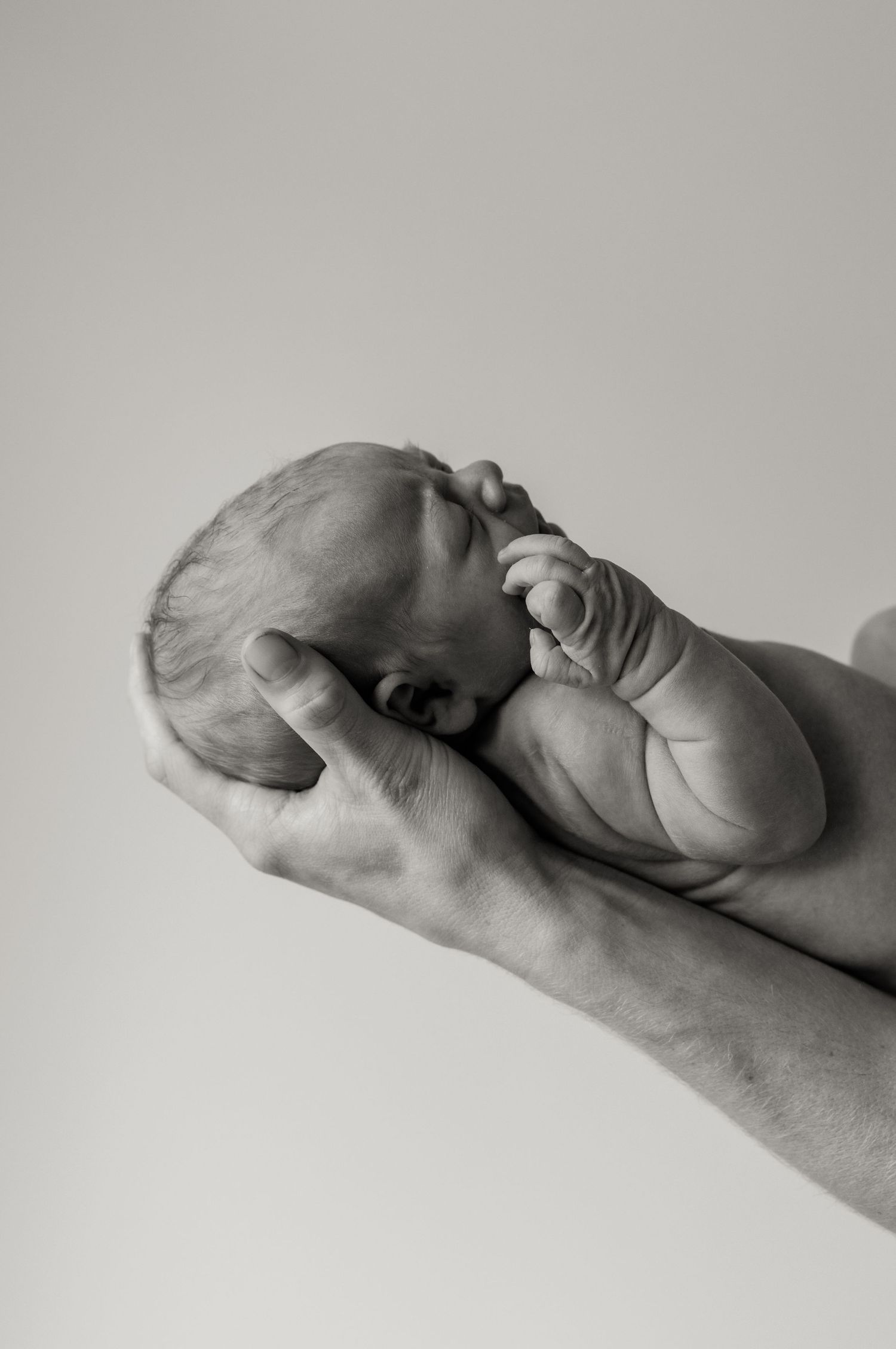 Black and white image of a newborn baby sleeping in dad's arms, his hand resting on his face.