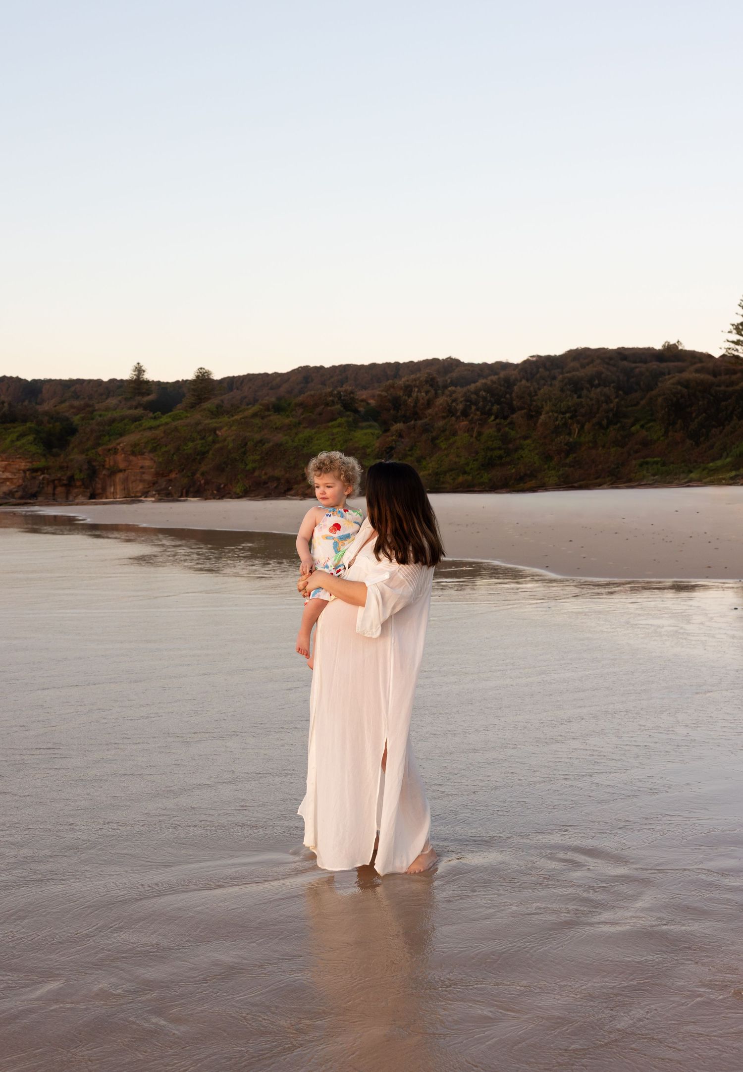 Mother talks to child with trees and caves of Lake Macquarie Caves Beach in the background.