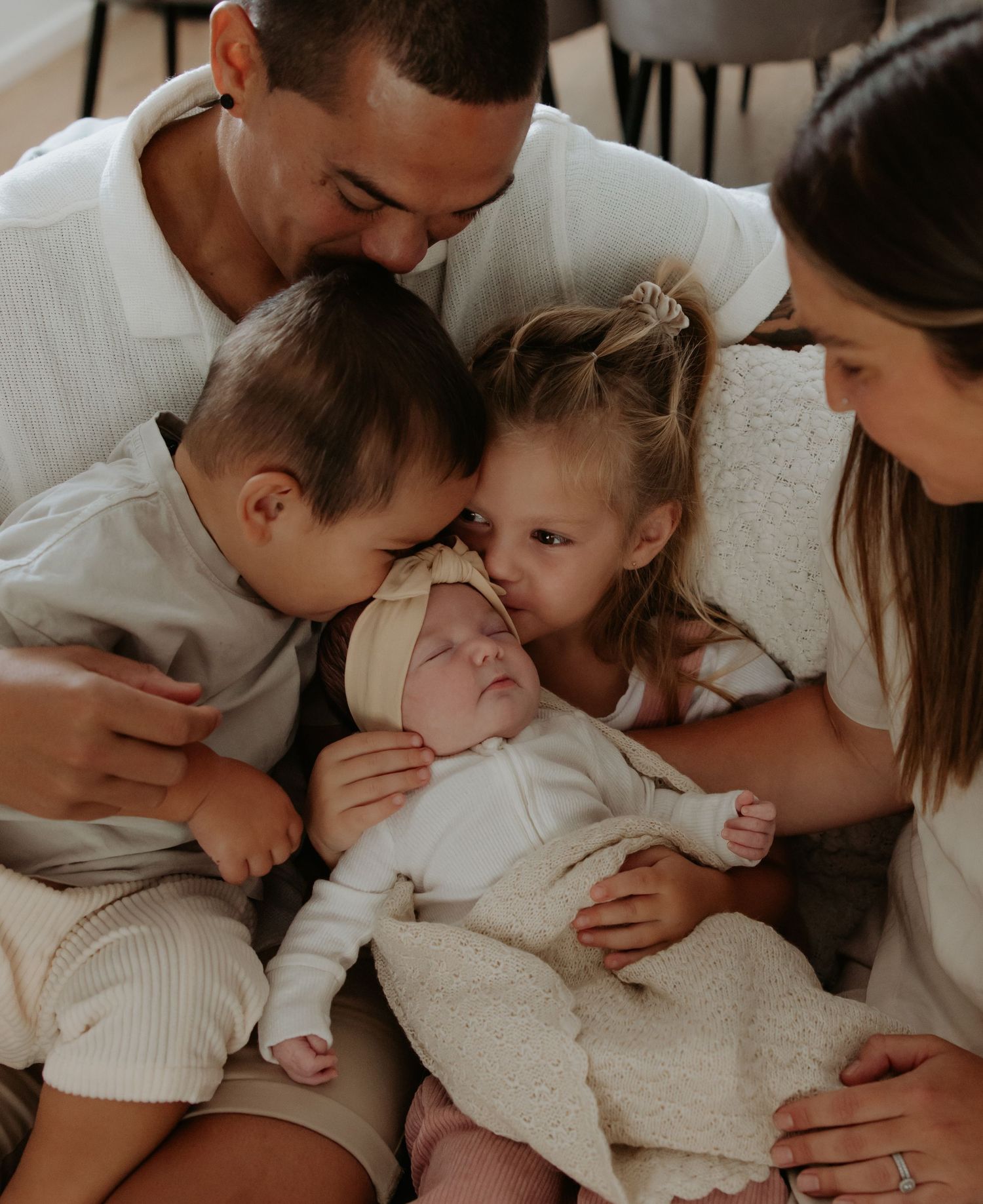 Family of five all gather around and look at their newest member. The siblings share a beautiful bond moment.