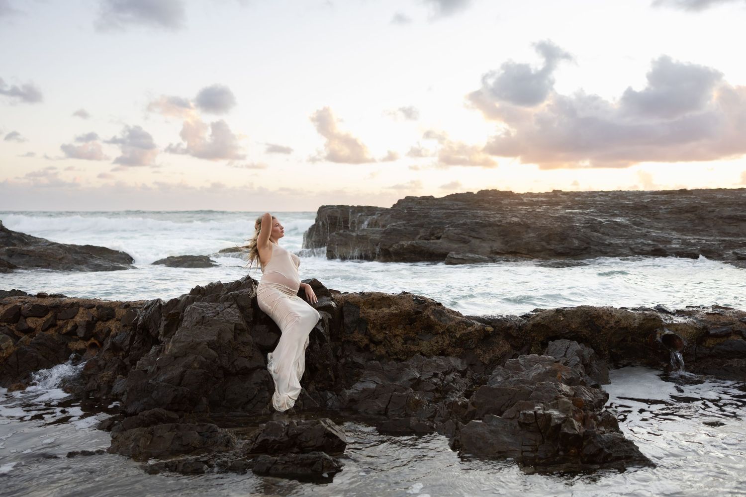 Woman looks towards the sunrise over the rocks at the beach.