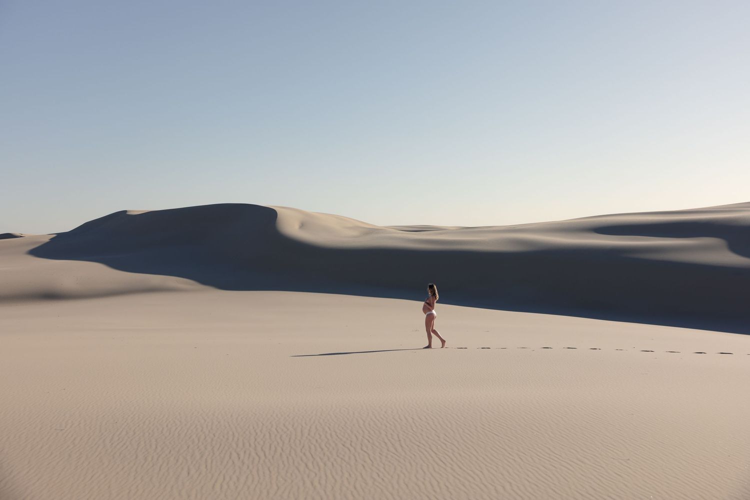 Pregnant mum walking across wide sand dunes at sunrise in Newcastle, Australia.