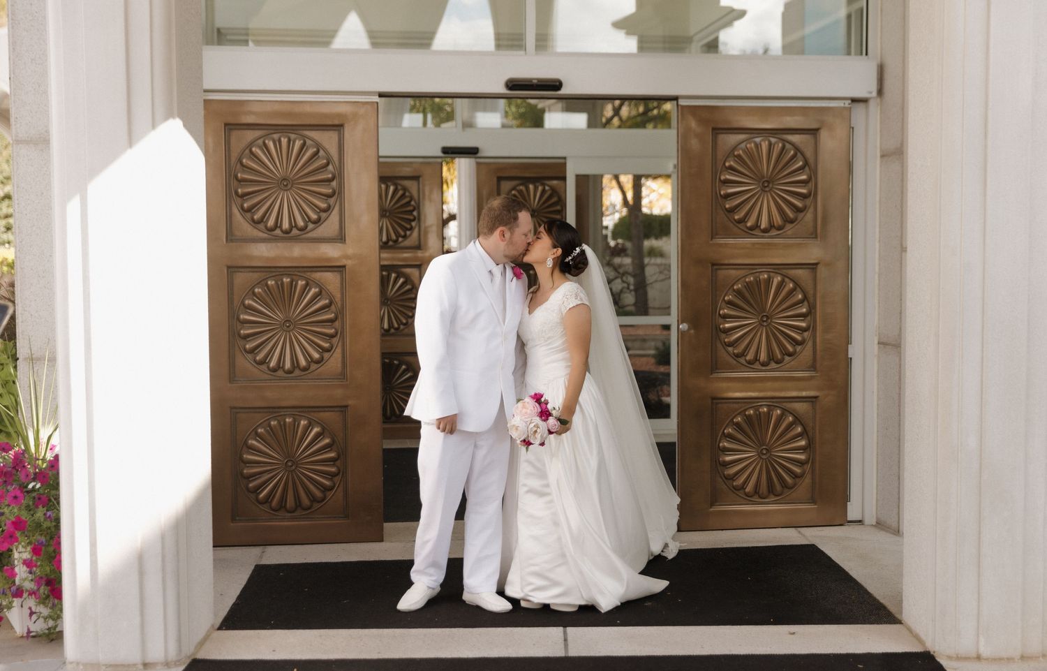 Elegant white temple building with ornate carved wooden doors serves as backdrop for wedding photos.