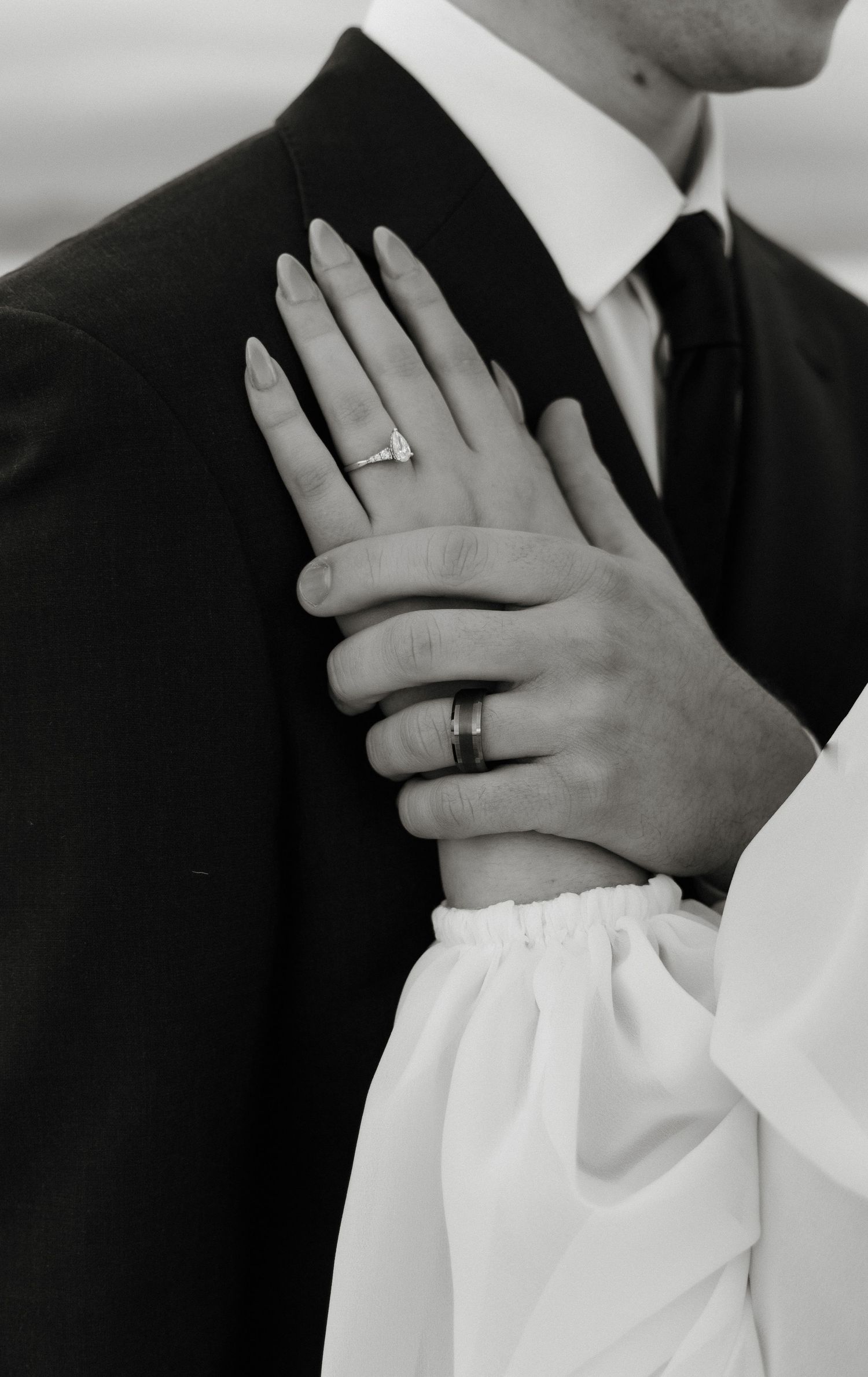 Wedding rings displayed on hands in black and white formal attire.