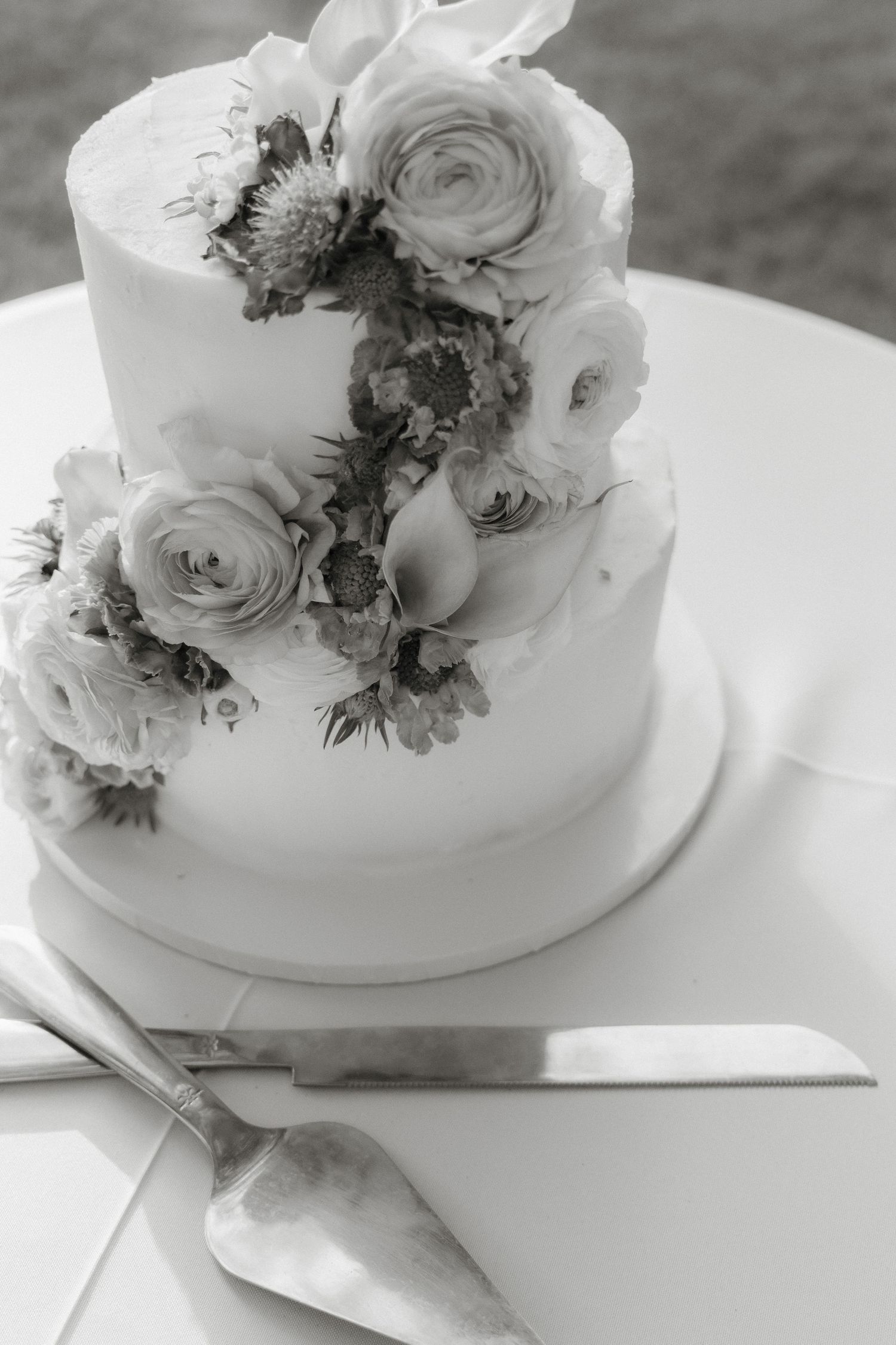 White tiered wedding cake adorned with delicate roses and greenery on a light surface.